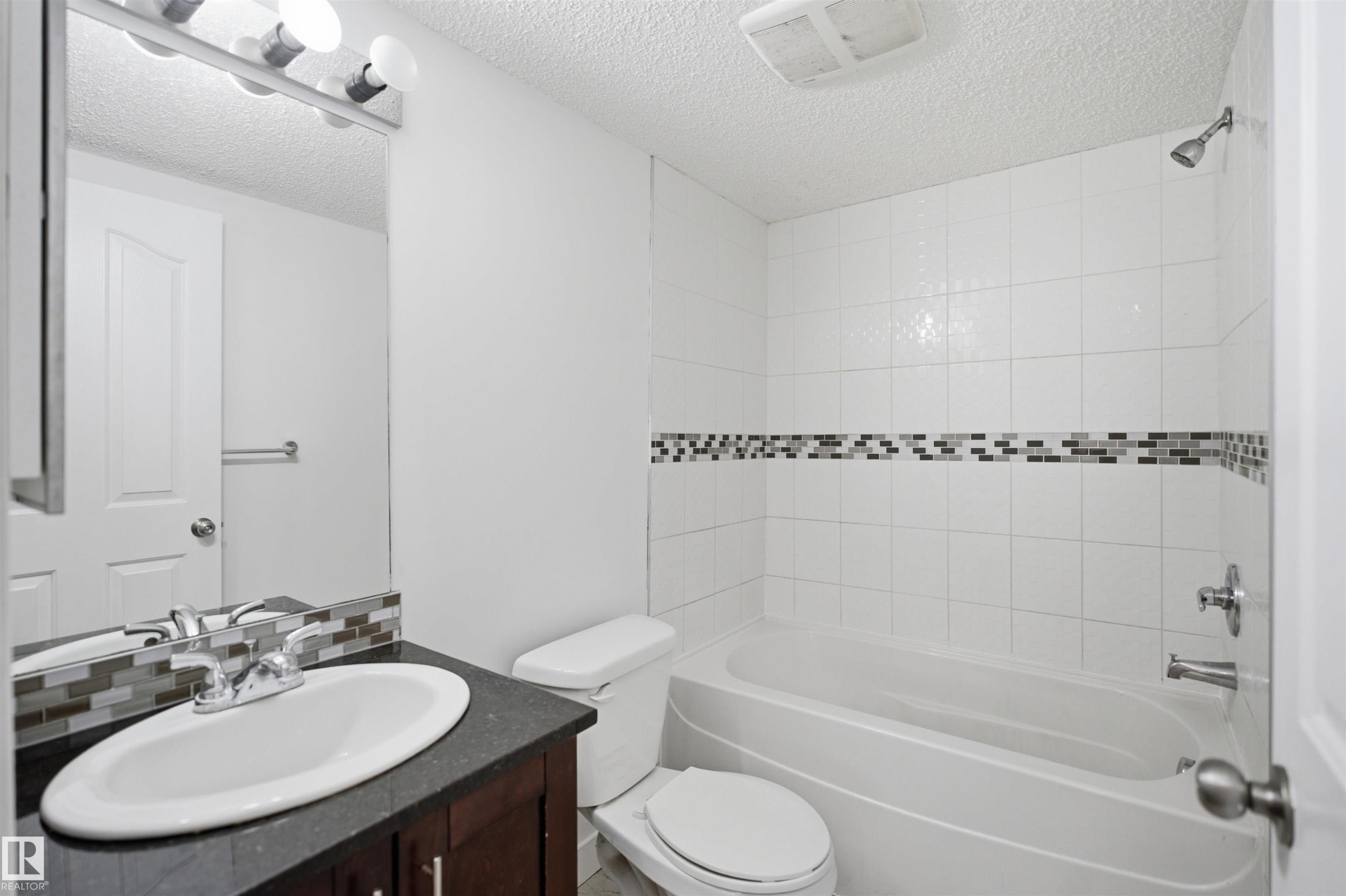 Bathroom featuring a dark wood-finish vanity with a white oval sink, chrome faucet, and dark countertop - 115 274 Mcconachie Drive, Edmonton, AB