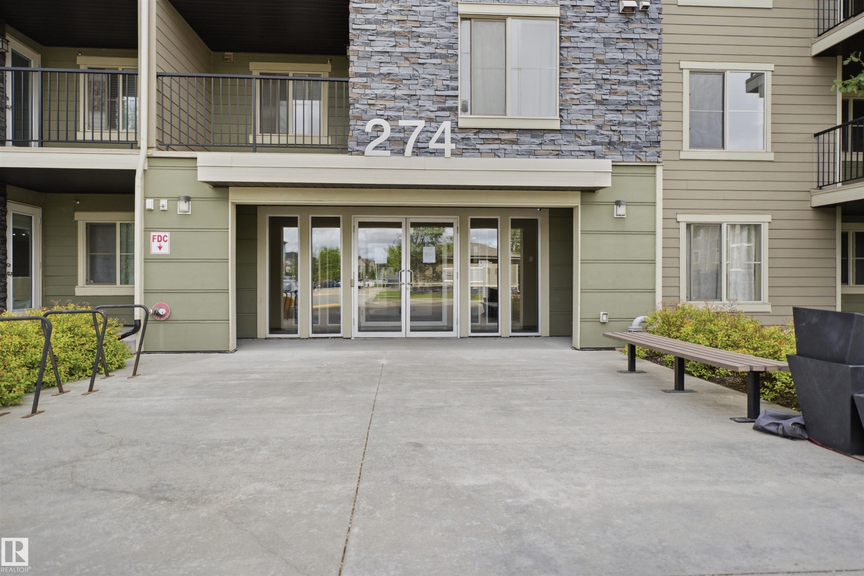 Building exterior featuring a stone facade accent, horizontal siding, and multiple balconies with dark railings - 115 274 Mcconachie Drive, Edmonton, AB