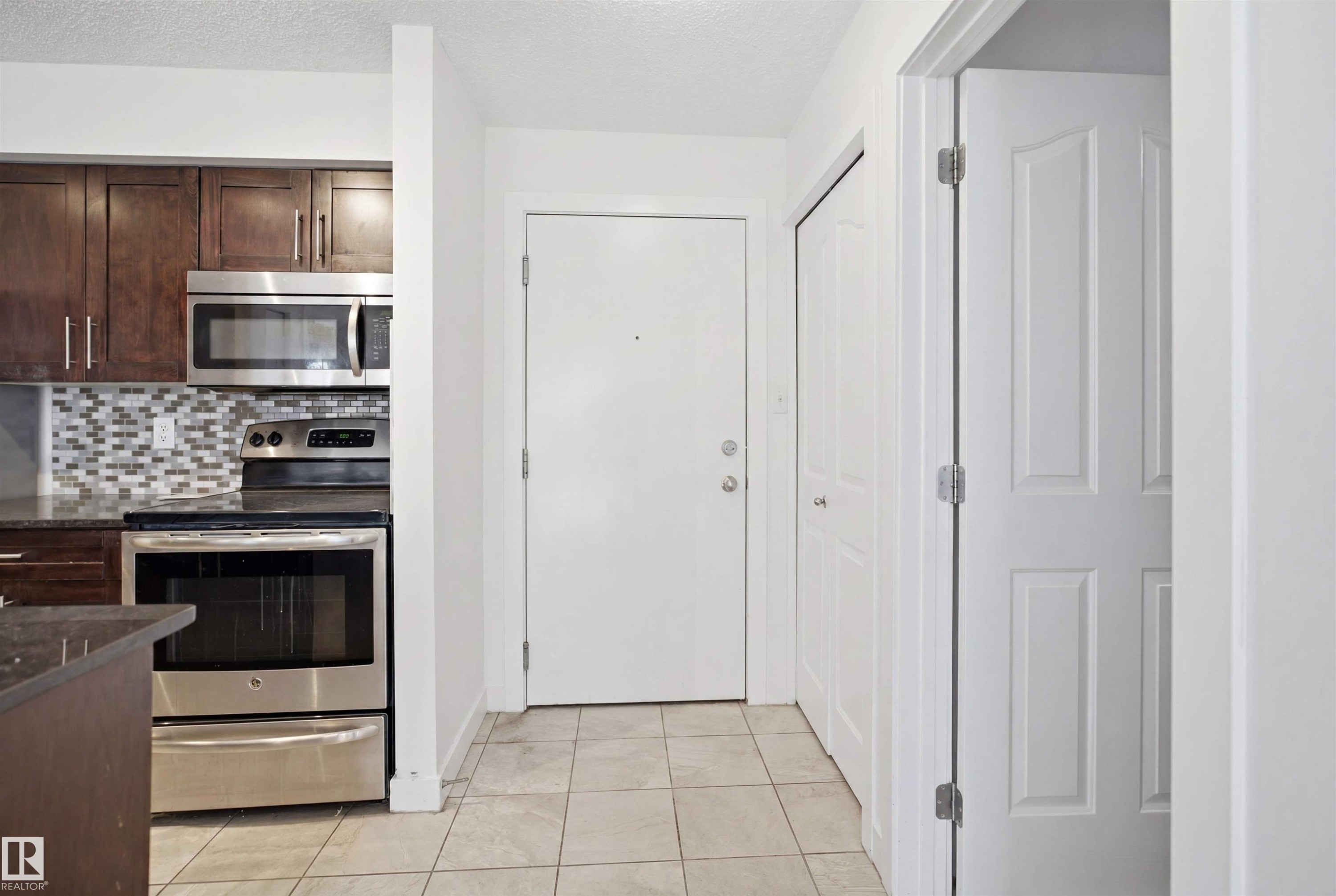 Kitchen area featuring dark wood-finish cabinetry, stainless steel appliances, and a mosaic tile backsplash - 115 274 Mcconachie Drive, Edmonton, AB