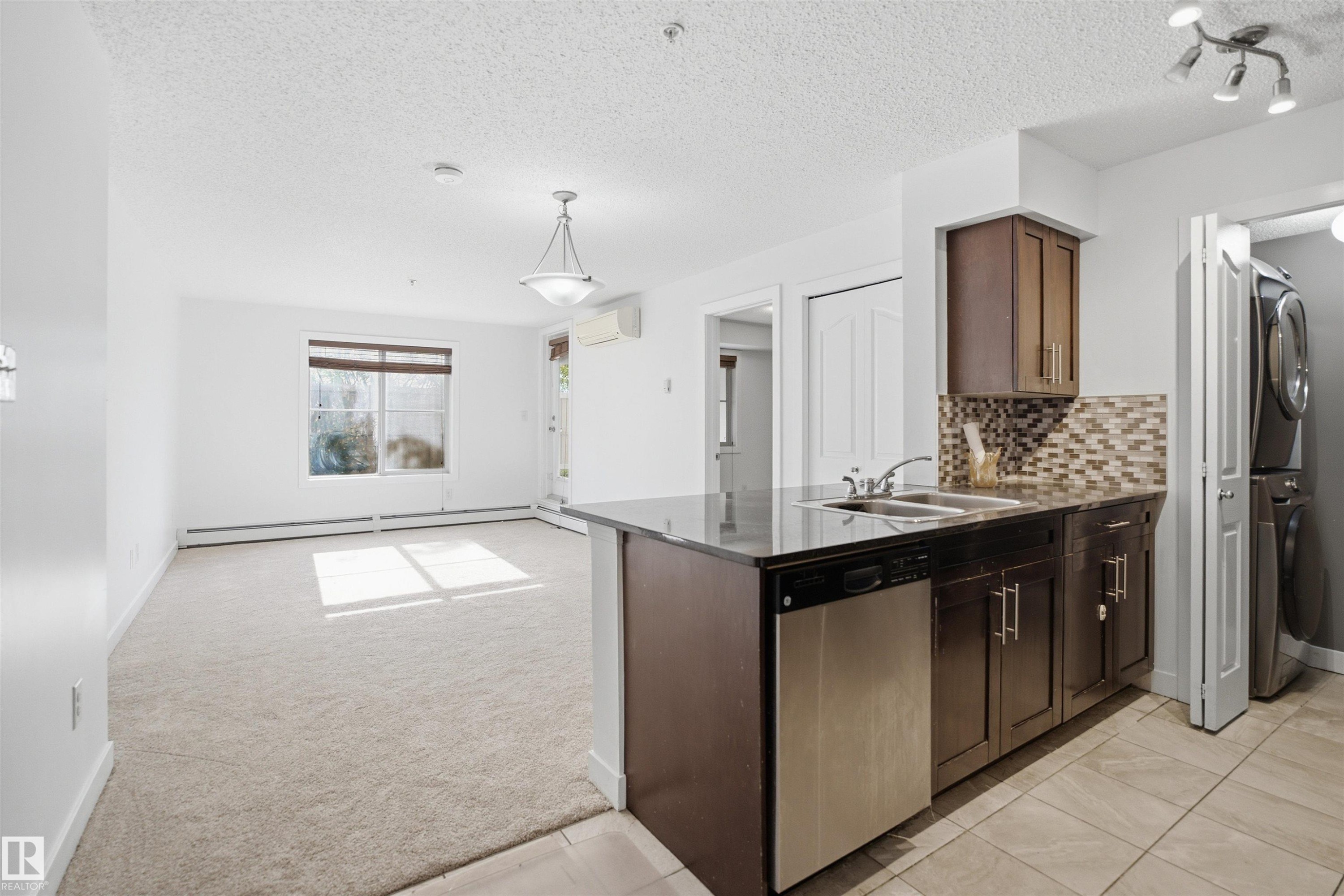 Open-concept living space featuring a kitchen with dark cabinetry, stainless steel dishwasher, and a tile backsplash - 115 274 Mcconachie Drive, Edmonton, AB