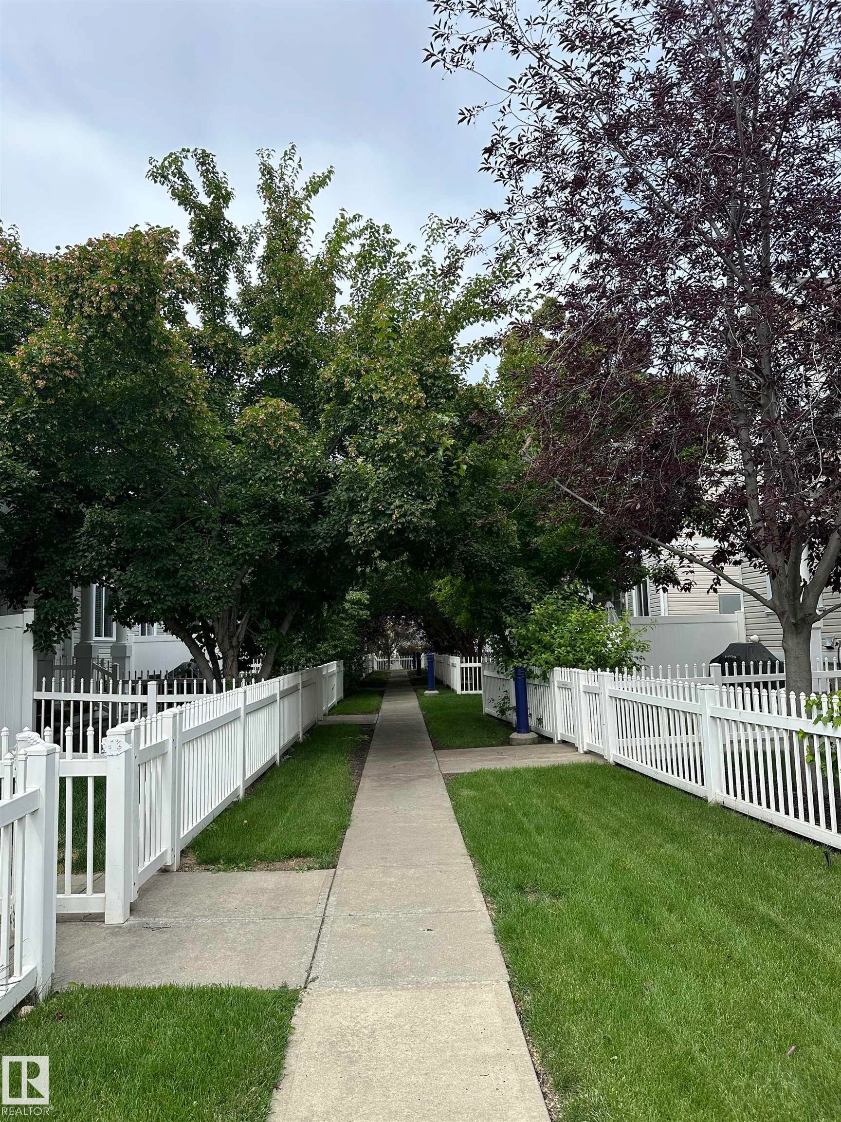 Concrete pathway bordered by green lawn and white picket fencing - #31 1804 70 St Sw, Edmonton, AB - Outdoor