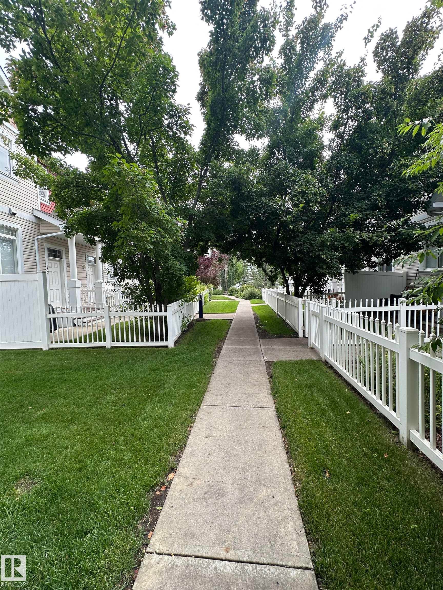 Paved walkway bordered by manicured green lawns and white picket fencing - #31 1804 70 St Sw, Edmonton, AB - Outdoor