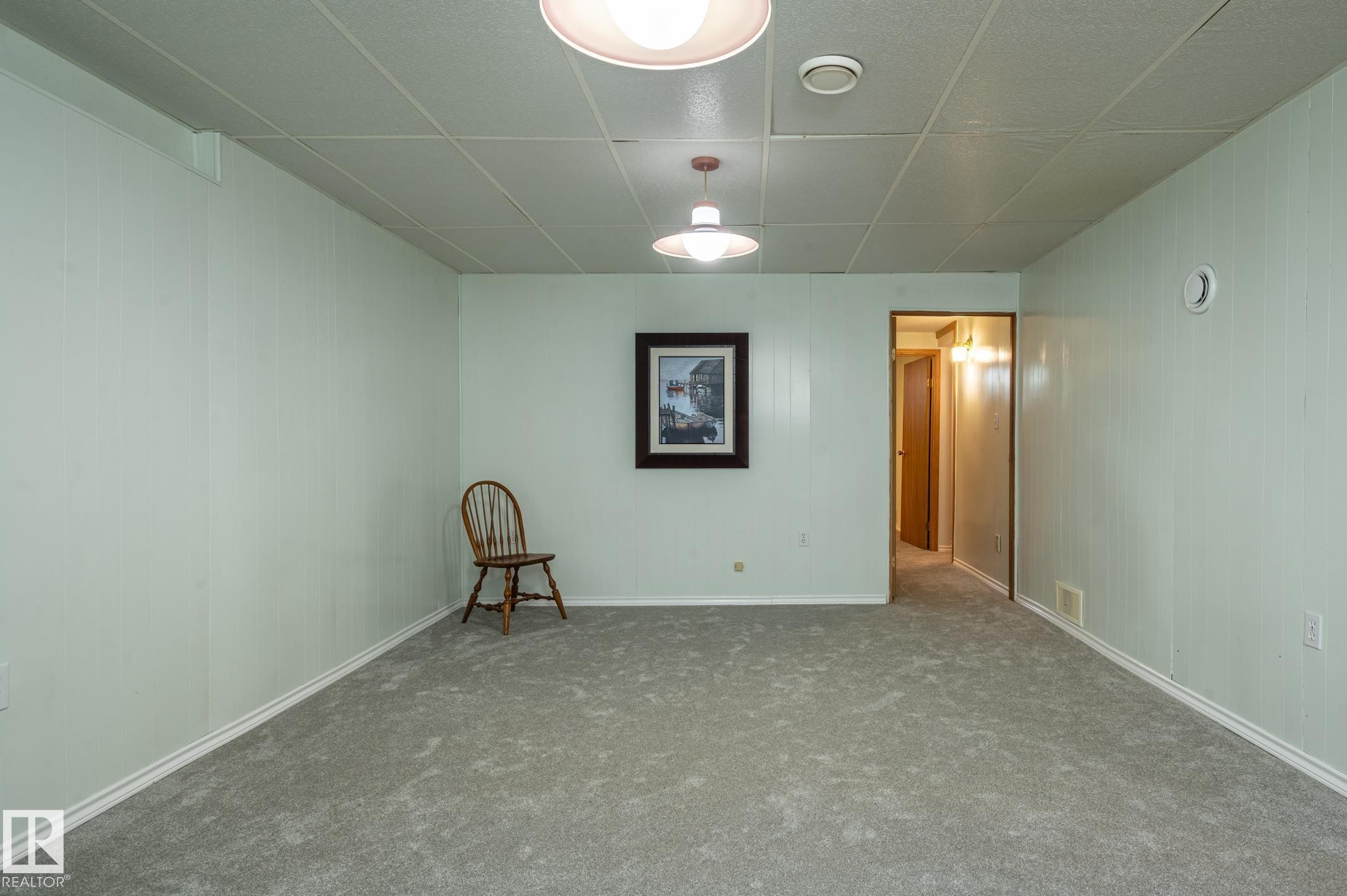 Spacious room featuring light-colored vertical paneling, grey carpet flooring, and a dropped ceiling with recessed lighting - 14708 108 Av, Edmonton, AB