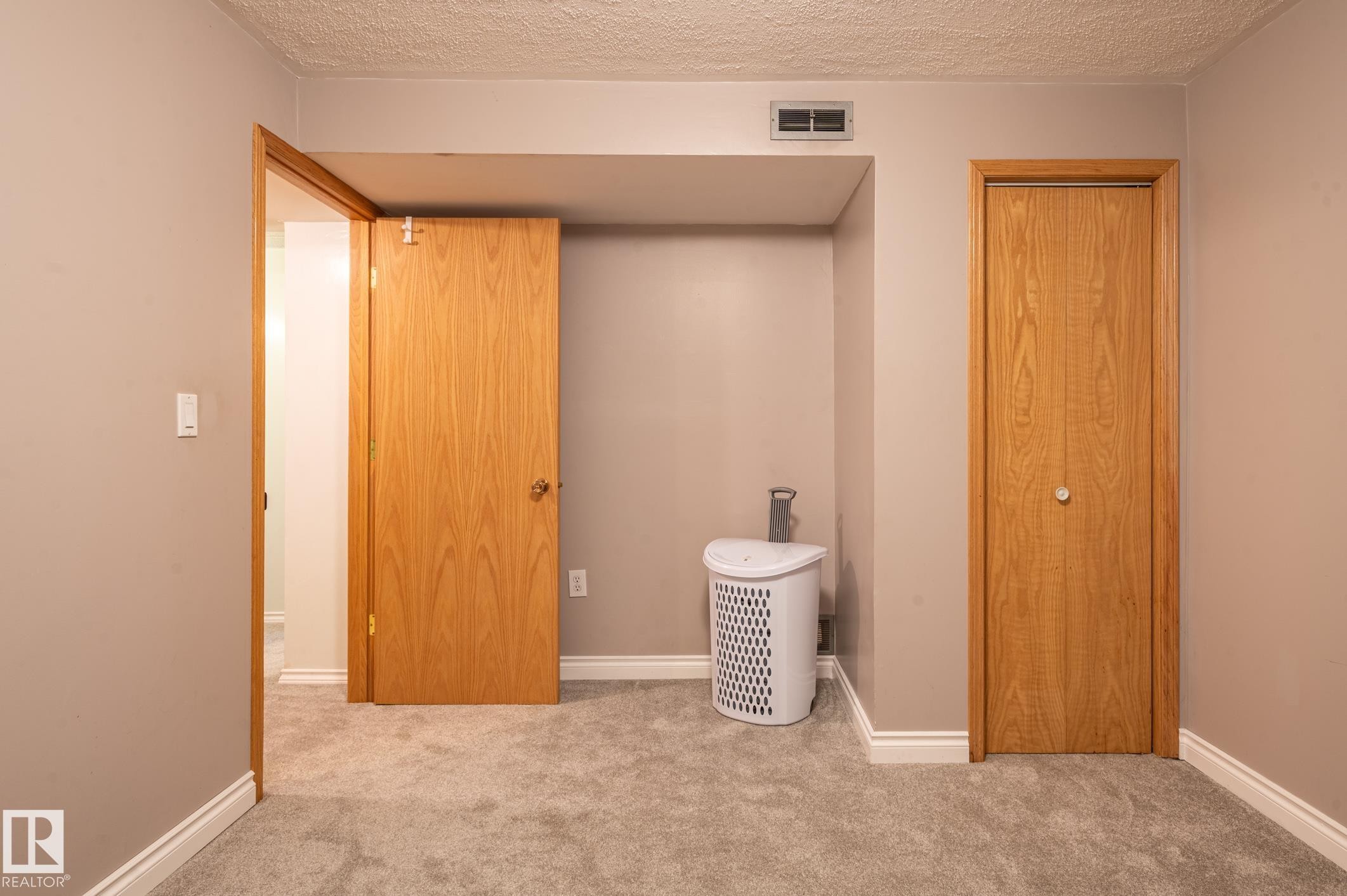 Carpeted interior space featuring light neutral wall paint, white baseboards, and two wood-finish doors - 14708 108 Av, Edmonton, AB