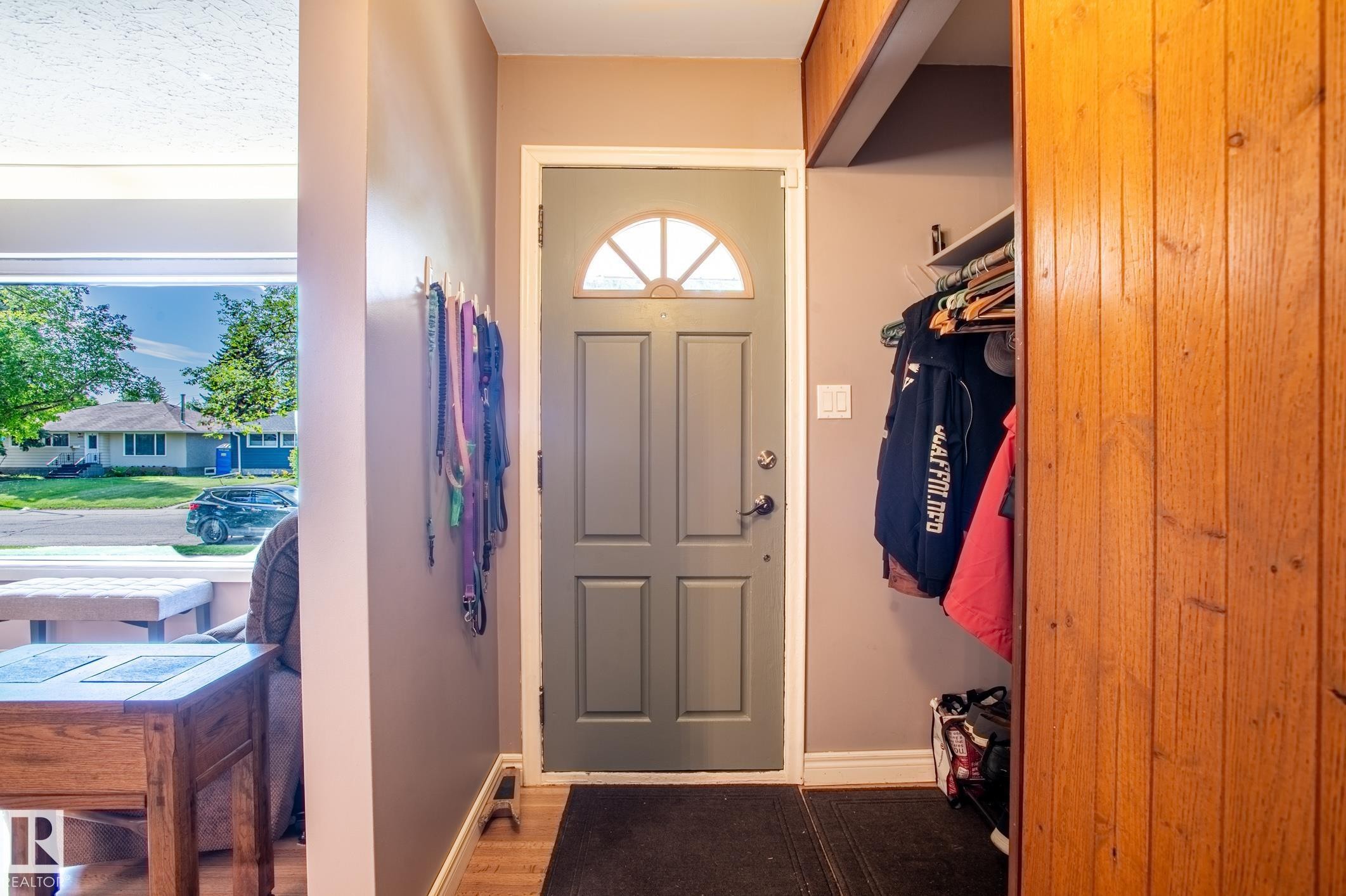 Entryway featuring a paneled door with a half-moon glass insert, wood-finish flooring, and a built-in closet with sliding wood panel doors - 14708 108 Av, Edmonton, AB