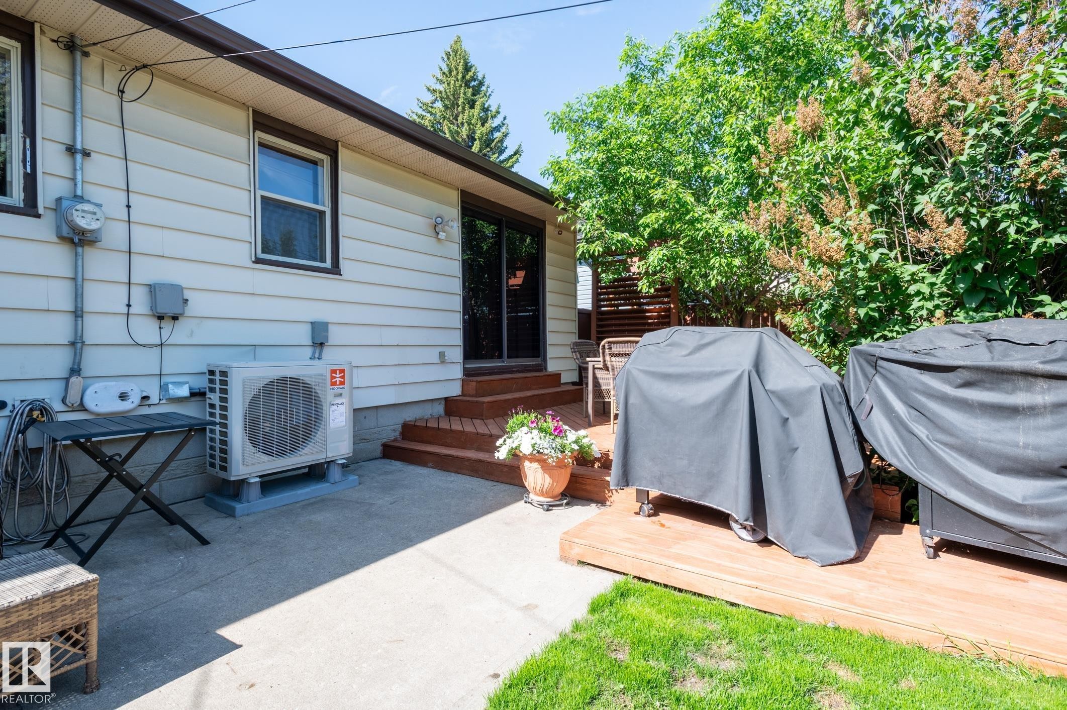 Rear exterior featuring a concrete patio, wood deck, and green lawn - 14708 108 Av, Edmonton, AB