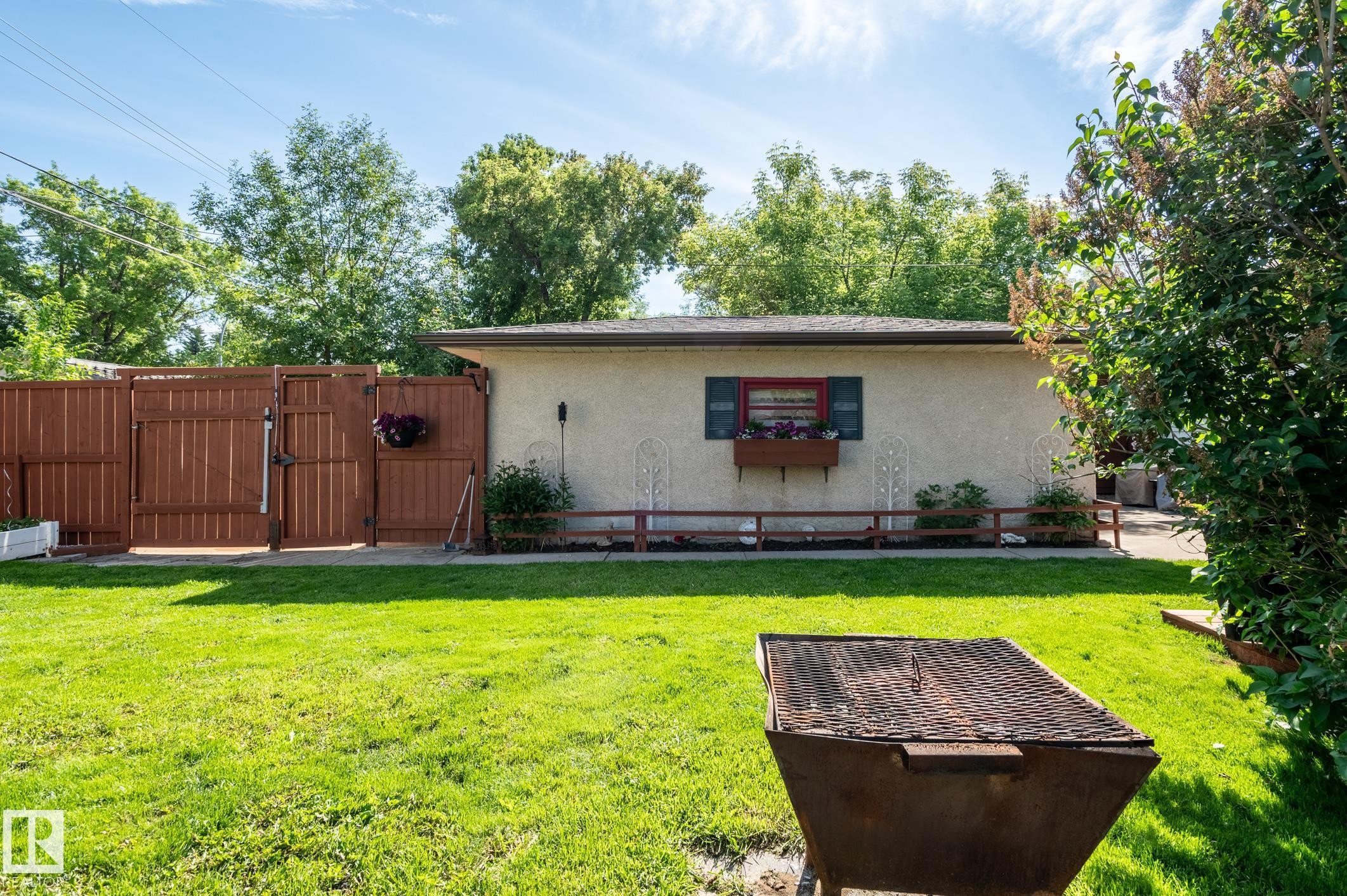 Spacious backyard featuring a manicured lawn, full-height privacy fencing, and a stucco-exterior outbuilding with a window box and decorative shutters - 14708 108 Av, Edmonton, AB