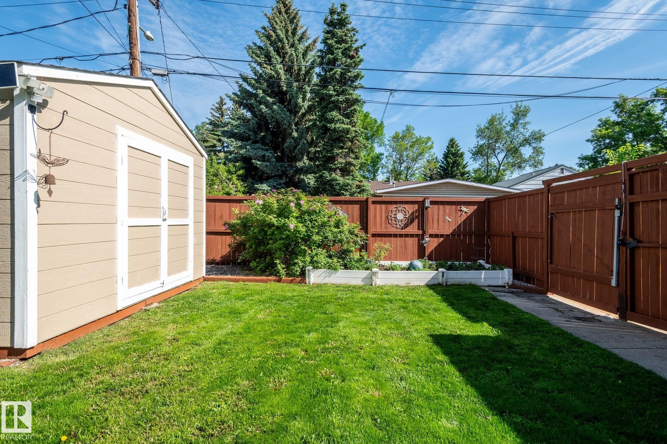 Expansive backyard featuring a manicured lawn, a detached storage shed, privacy fencing, and raised garden beds - 14708 108 Av, Edmonton, AB
