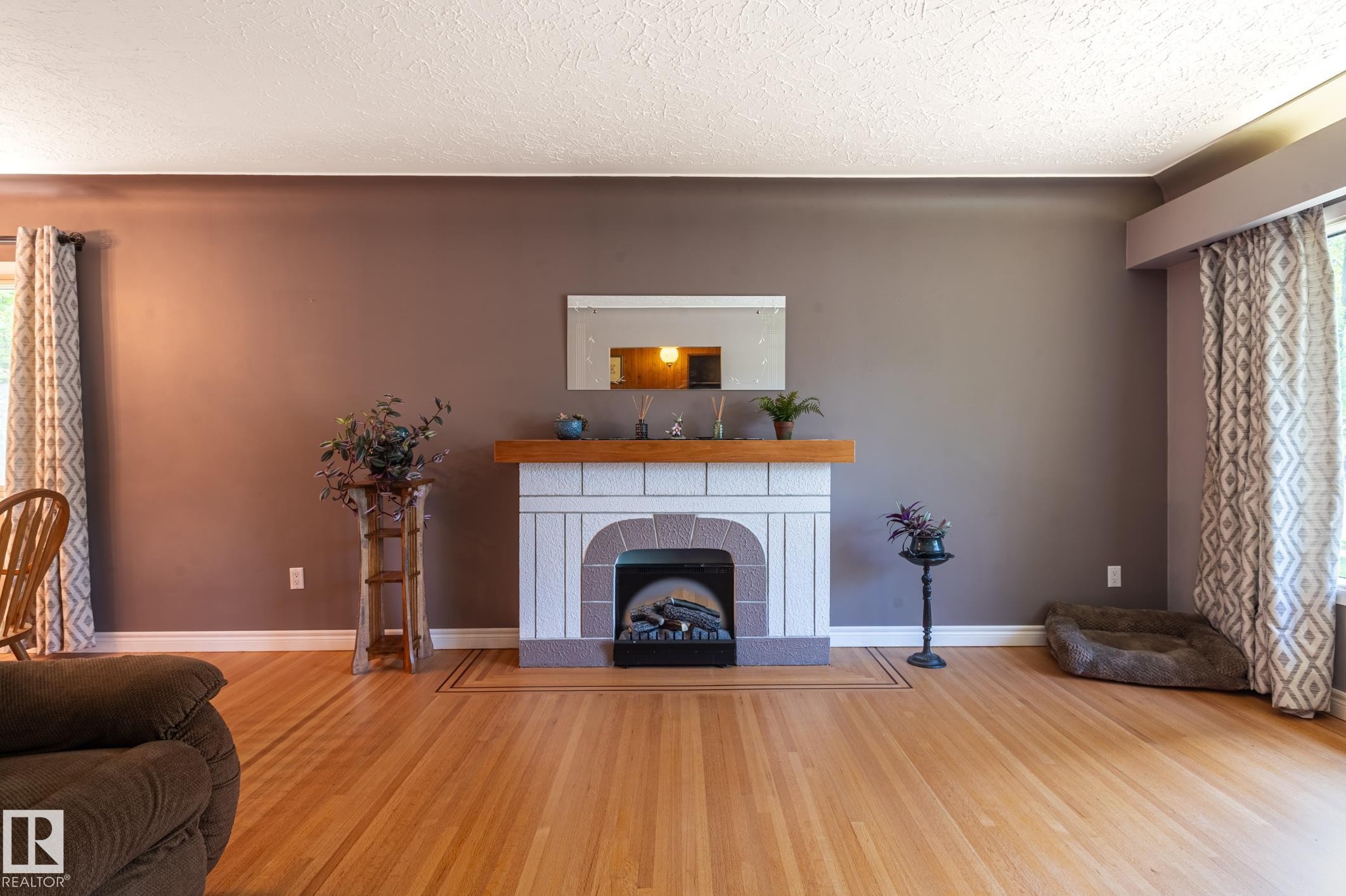 Hardwood flooring throughout the room, complemented by a white-tiled fireplace featuring a wood-finish mantel and an electric insert - 14708 108 Av, Edmonton, AB