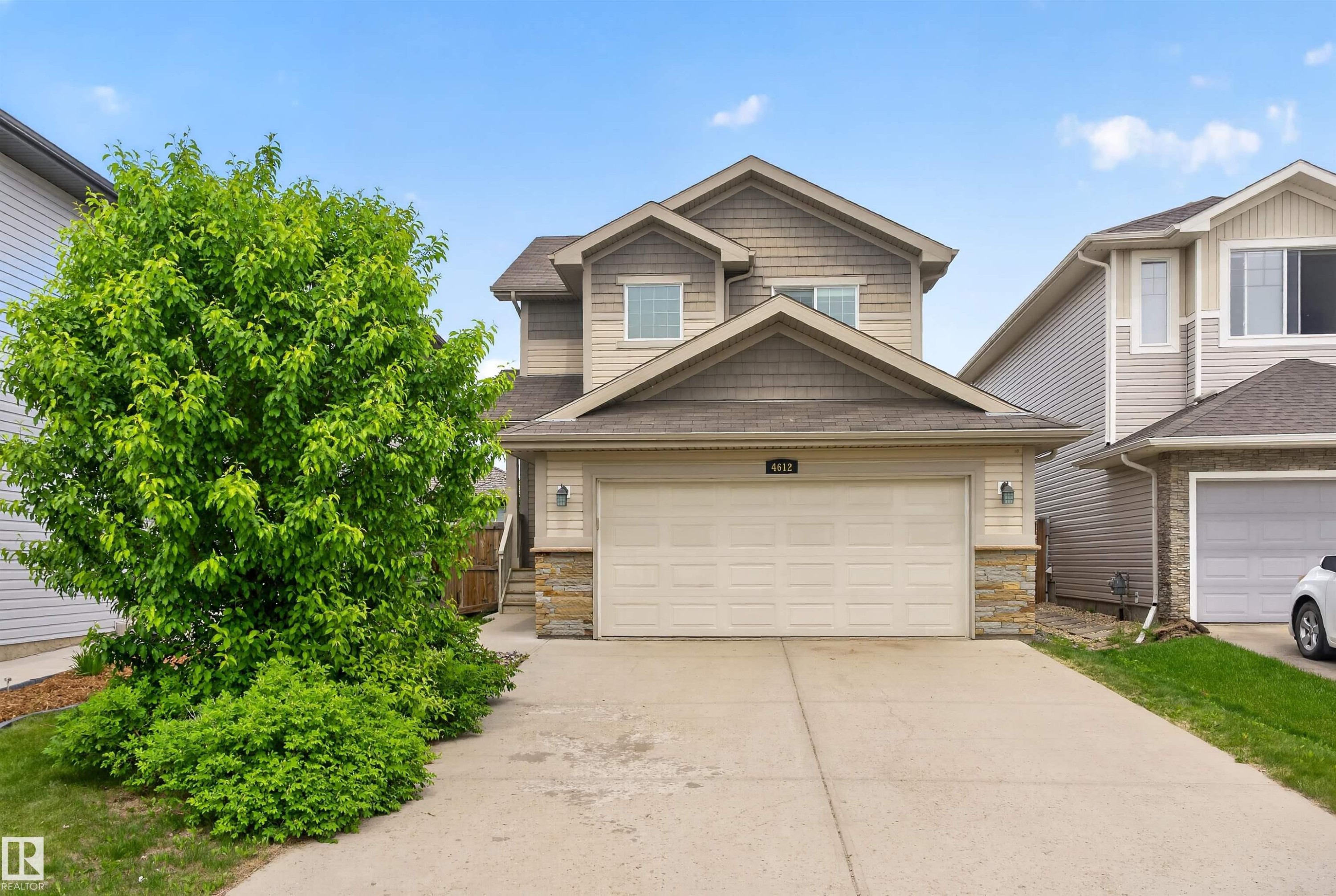 Two-story residence featuring light-colored siding, a prominent attached two-car garage, and stone accents - 4612 Westcliff Point(E), Edmonton, AB