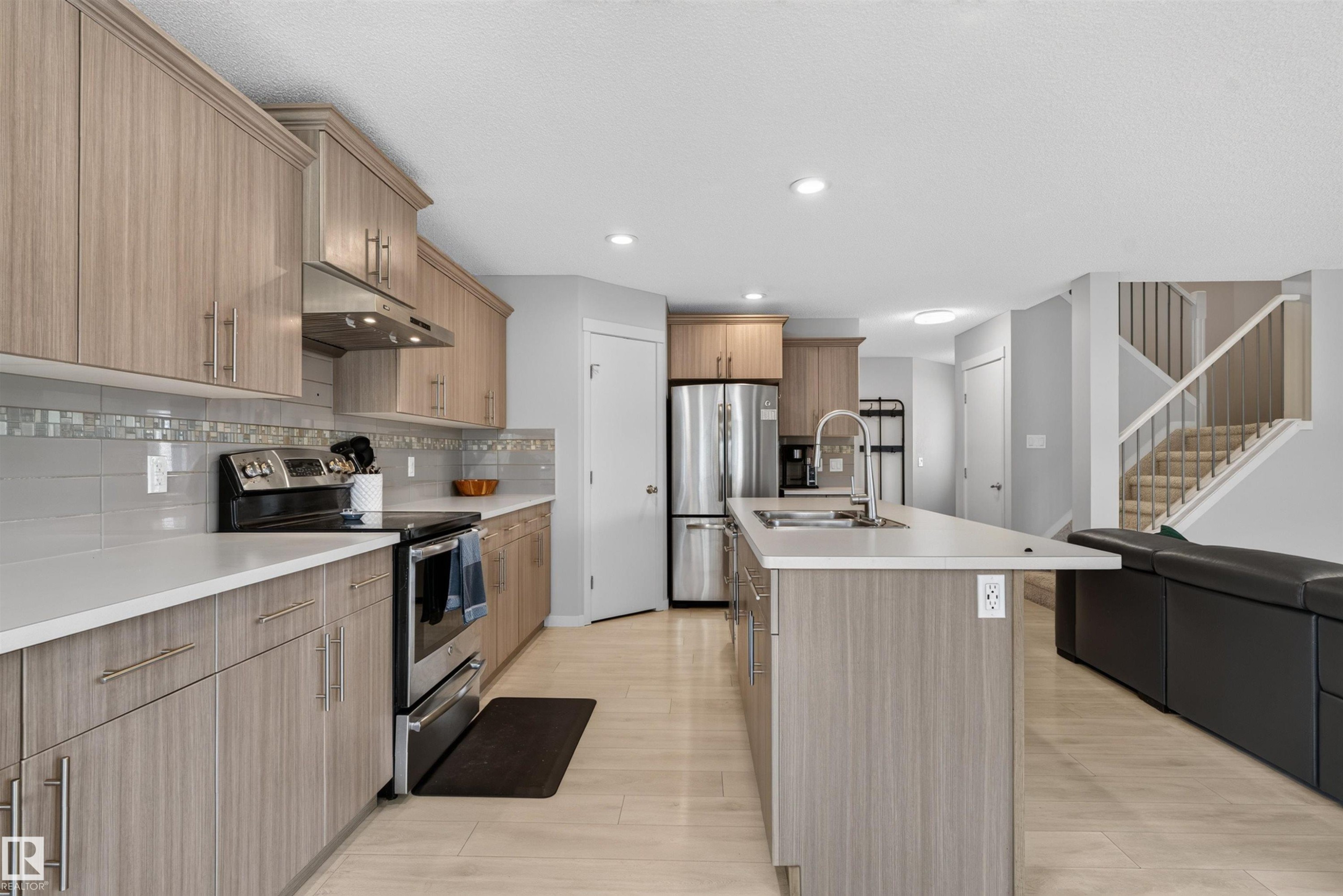 Kitchen featuring wood-finish cabinetry, stainless steel appliances, a center island with a sink, and light wood-finish flooring - 4612 Westcliff Point(E), Edmonton, AB