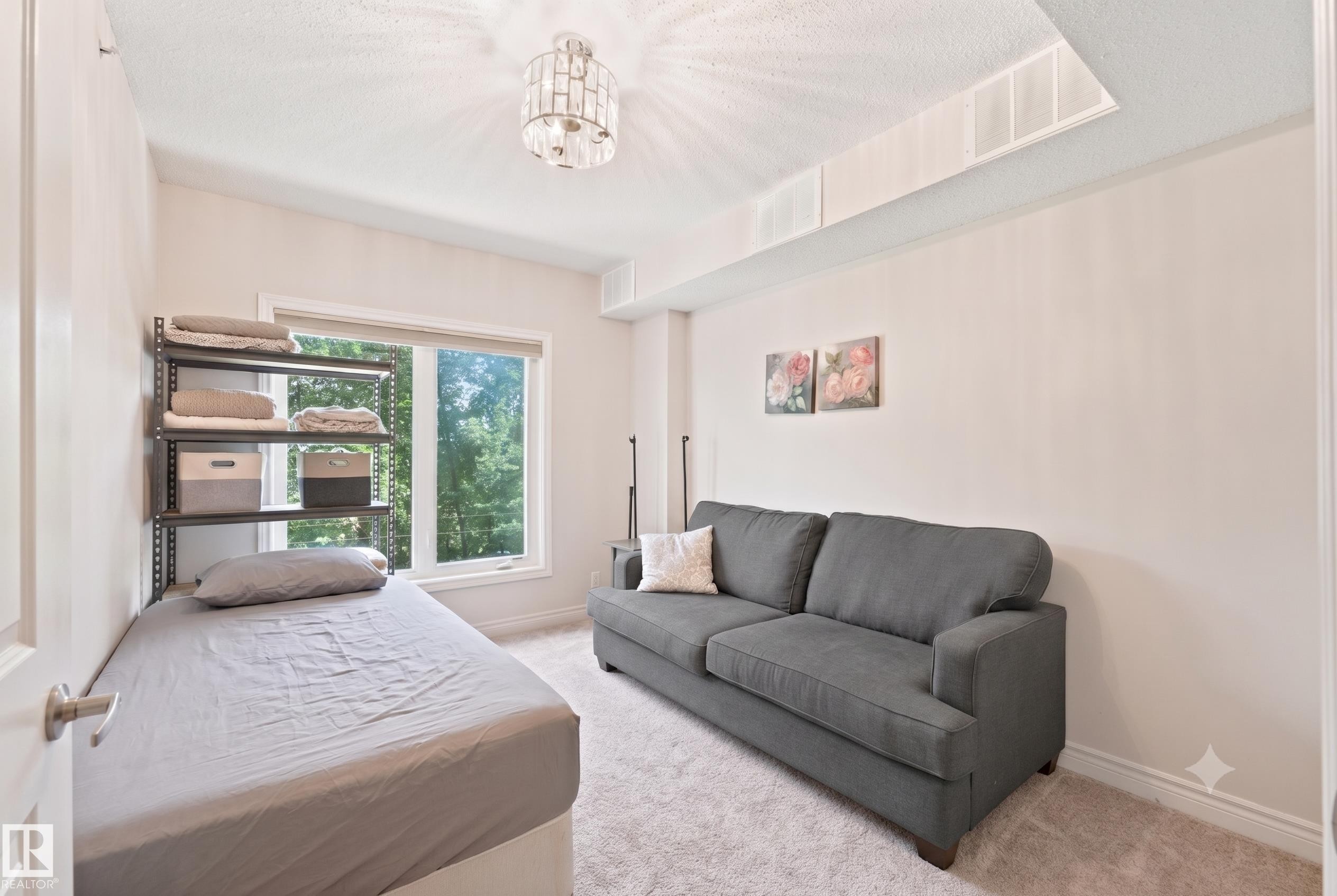 Bright room featuring a large window with exterior foliage, neutral wall tones, and plush carpeting - 305 11111 82 Avenue, Edmonton, AB