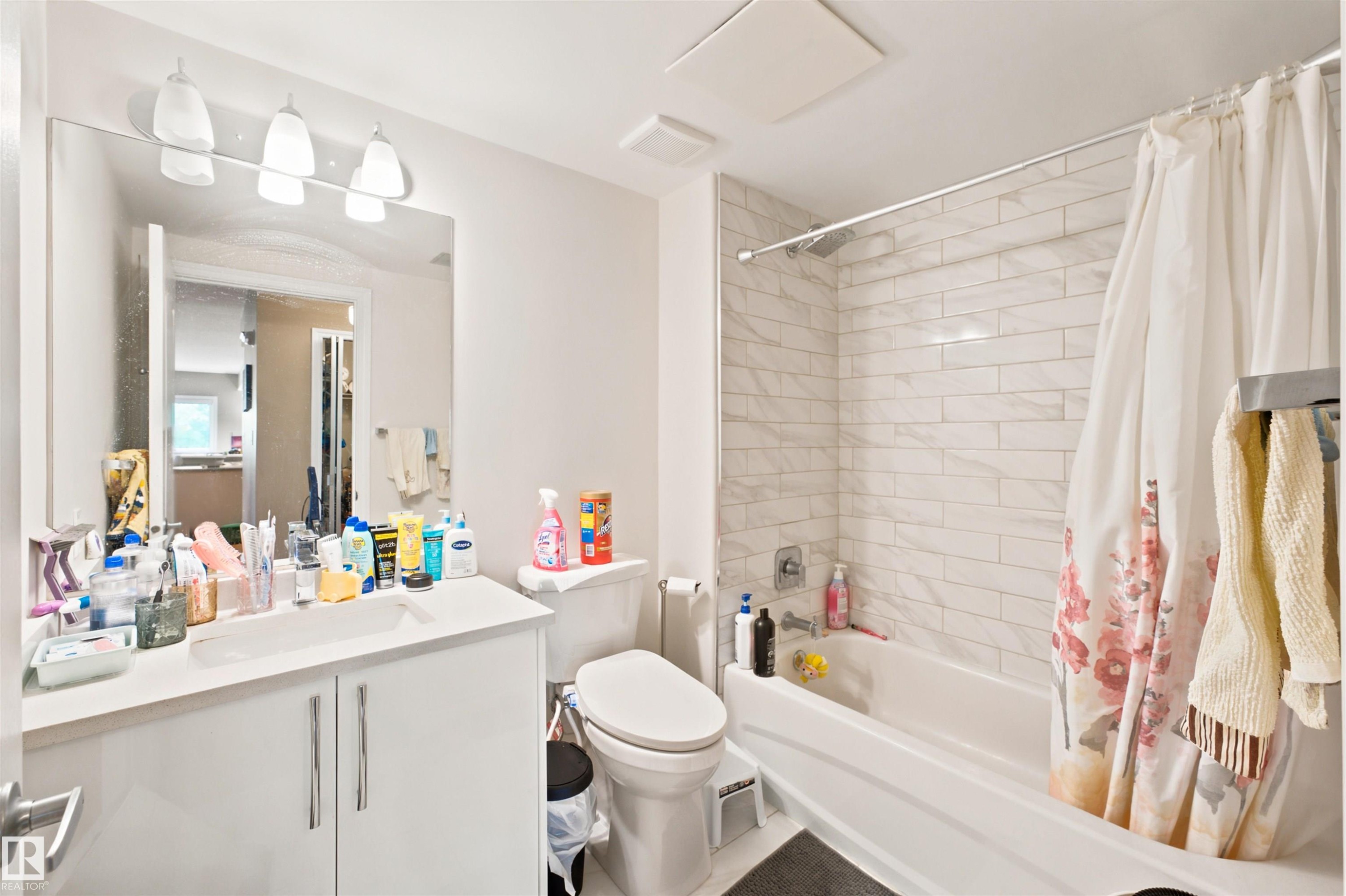 Bathroom featuring a white vanity with integrated sink, a large wall-mounted mirror, and a three-light fixture - 305 11111 82 Avenue, Edmonton, AB