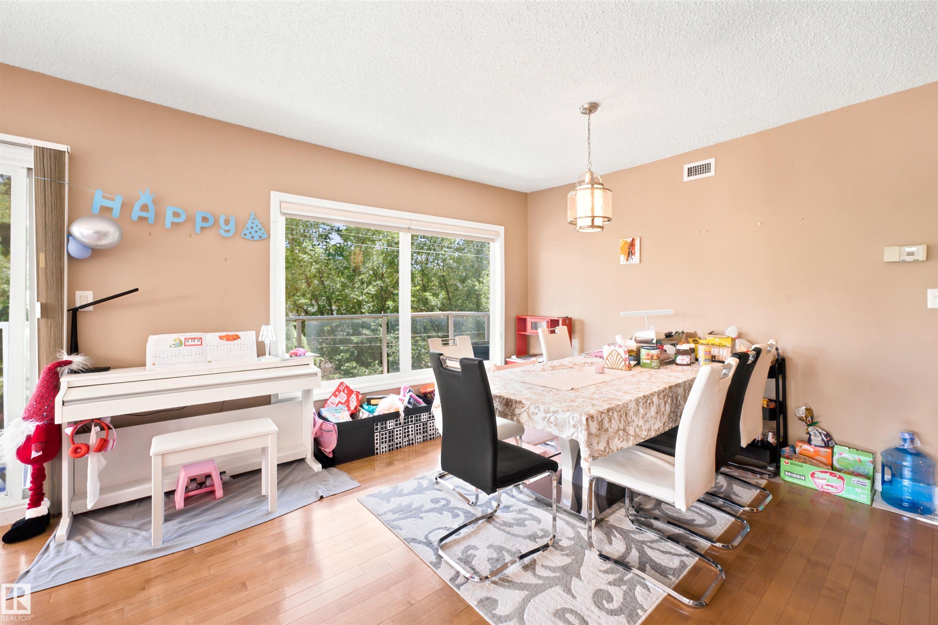 Dining area featuring wood-finish flooring, a contemporary ceiling light fixture, a large window, and a glass-paneled door - 305 11111 82 Avenue, Edmonton, AB
