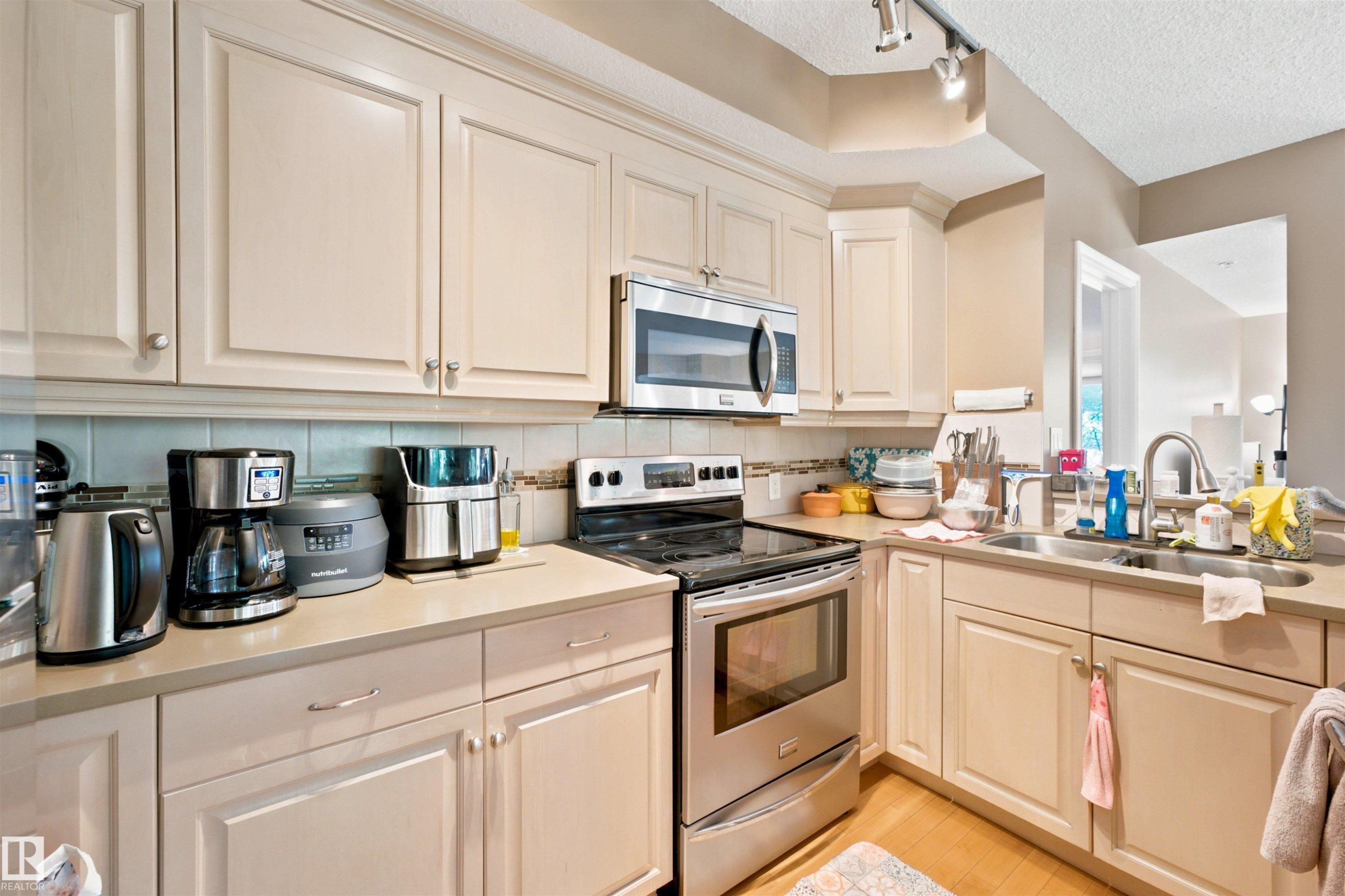 Kitchen featuring light-toned cabinetry, stainless steel appliances, a tile backsplash, and wood-finish flooring - 305 11111 82 Avenue, Edmonton, AB