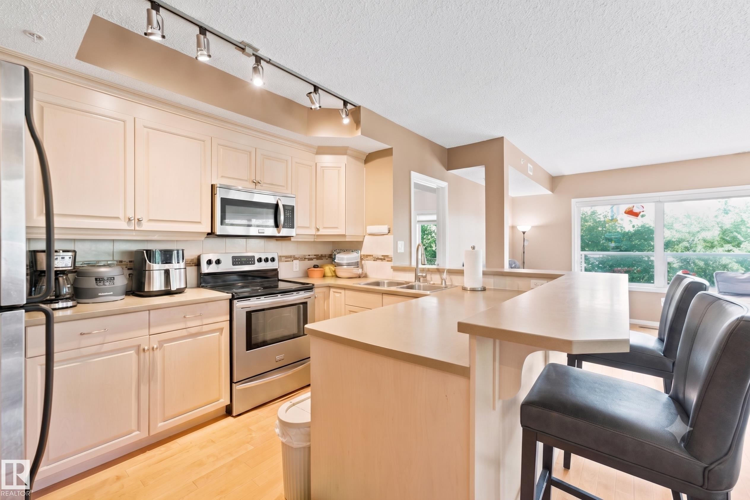 Kitchen featuring light wood-finish cabinetry, stainless steel appliances, a tile backsplash, and a breakfast bar with seating - 305 11111 82 Avenue, Edmonton, AB