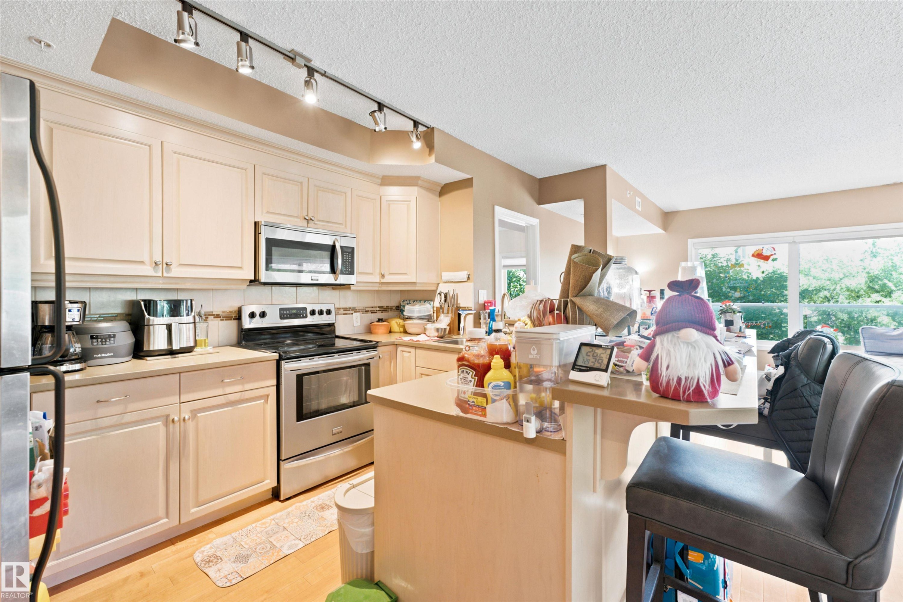 Kitchen featuring light-toned cabinetry, stainless steel appliances, a bar-height counter, and track lighting - 305 11111 82 Avenue, Edmonton, AB
