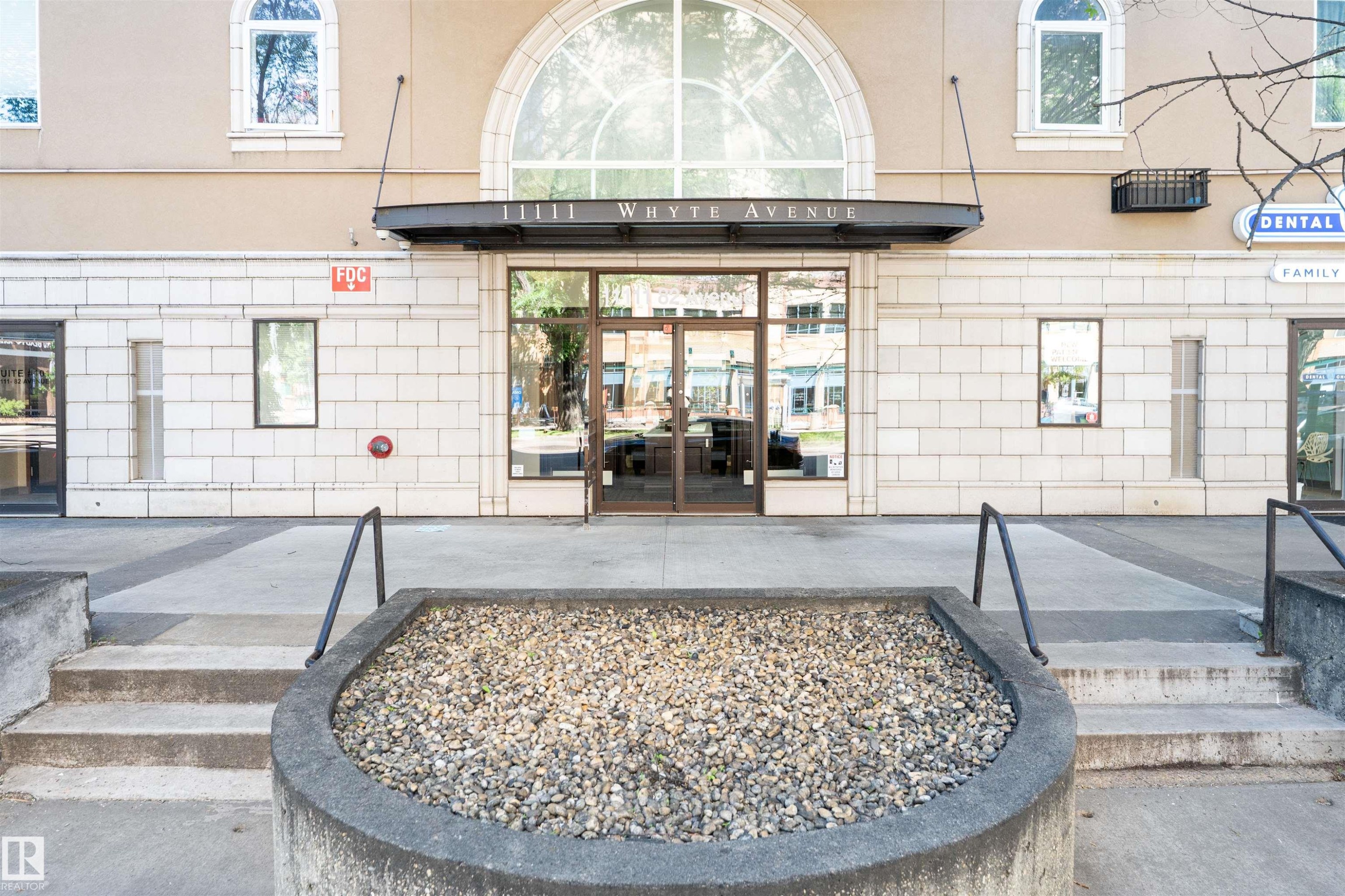 Building exterior featuring a prominent arched window, glass entry doors, and a stone facade - 305 11111 82 Avenue, Edmonton, AB