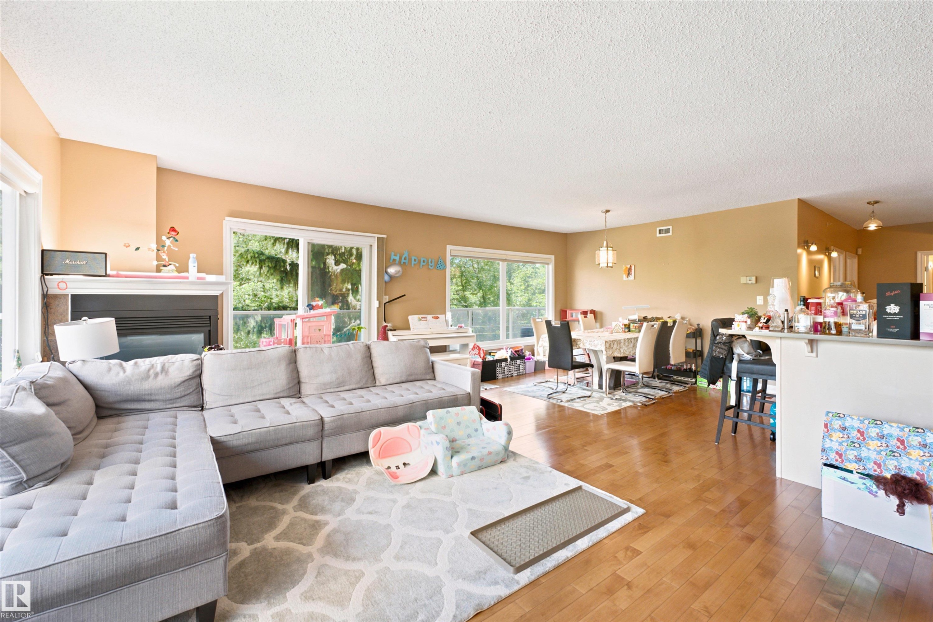 Open-concept living space featuring wood-finish flooring, a built-in fireplace with a white mantel, and multiple sliding glass doors - 305 11111 82 Avenue, Edmonton, AB
