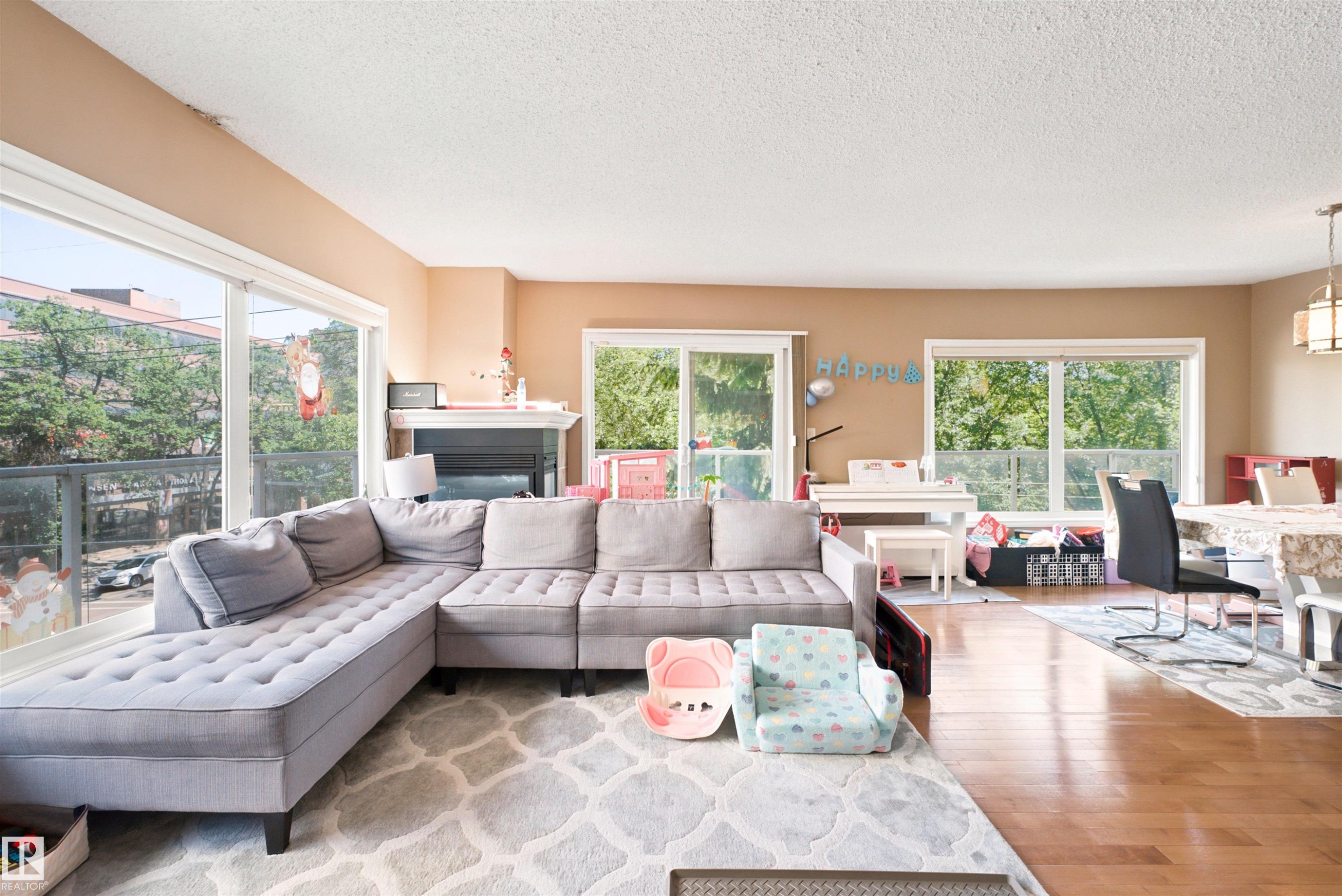 Living area featuring wood-finish flooring, a fireplace with a white mantel, and multiple large windows - 305 11111 82 Avenue, Edmonton, AB