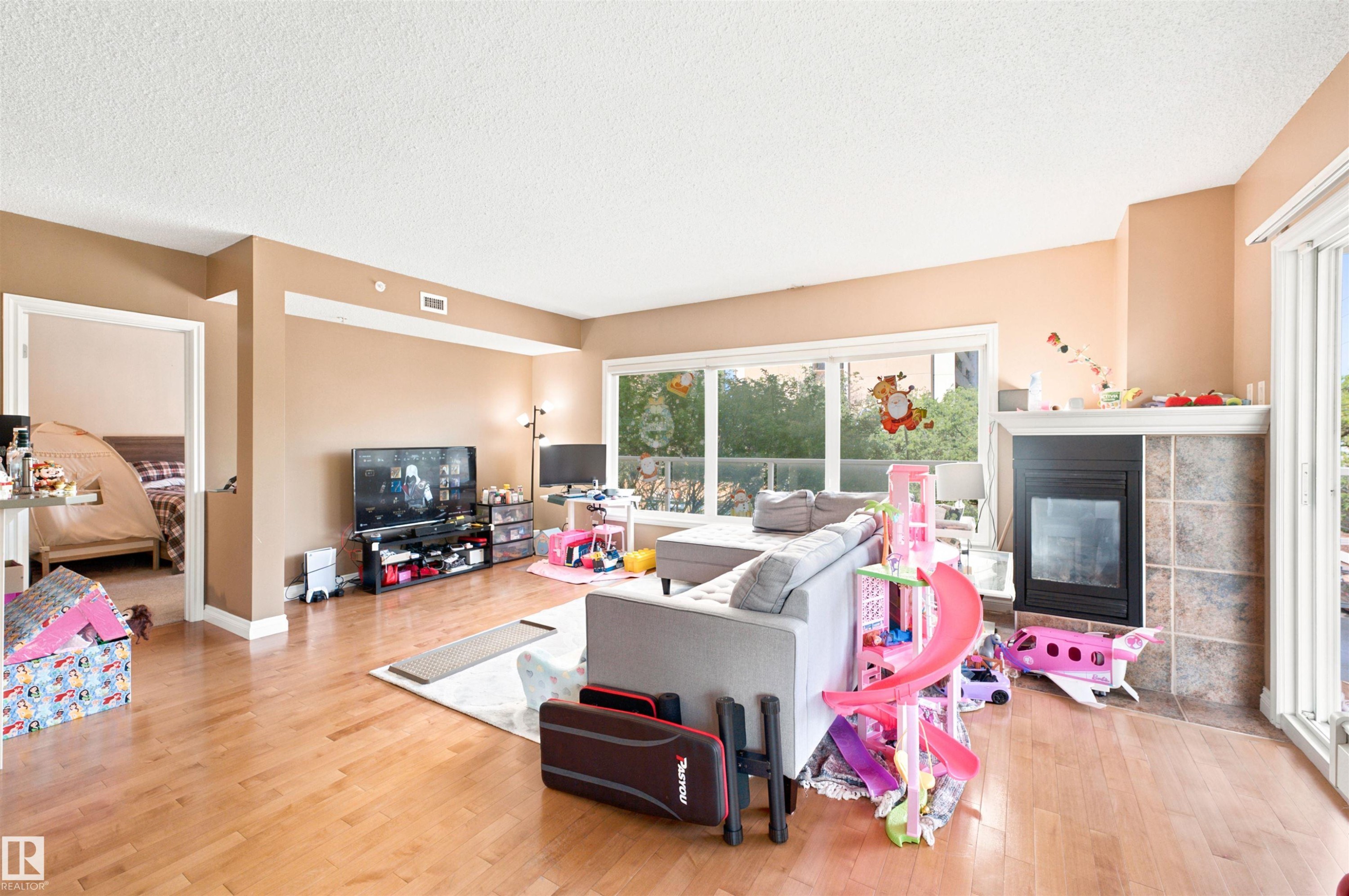 Spacious living area featuring wood-finish flooring, large windows, and a tiled fireplace - 305 11111 82 Avenue, Edmonton, AB