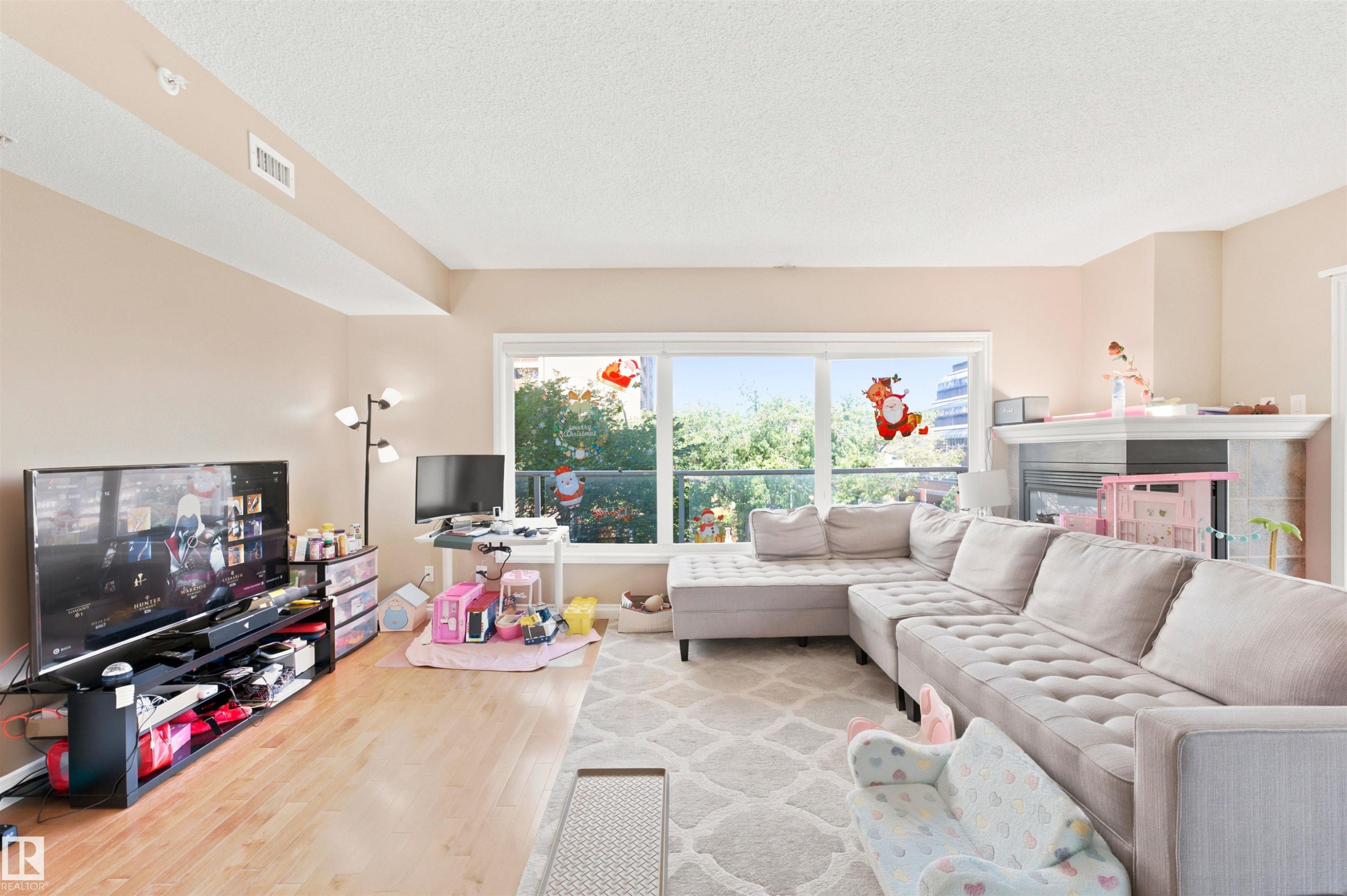 Spacious living area featuring large windows, wood-finish flooring, recessed lighting, and a fireplace with a stone surround - 305 11111 82 Avenue, Edmonton, AB