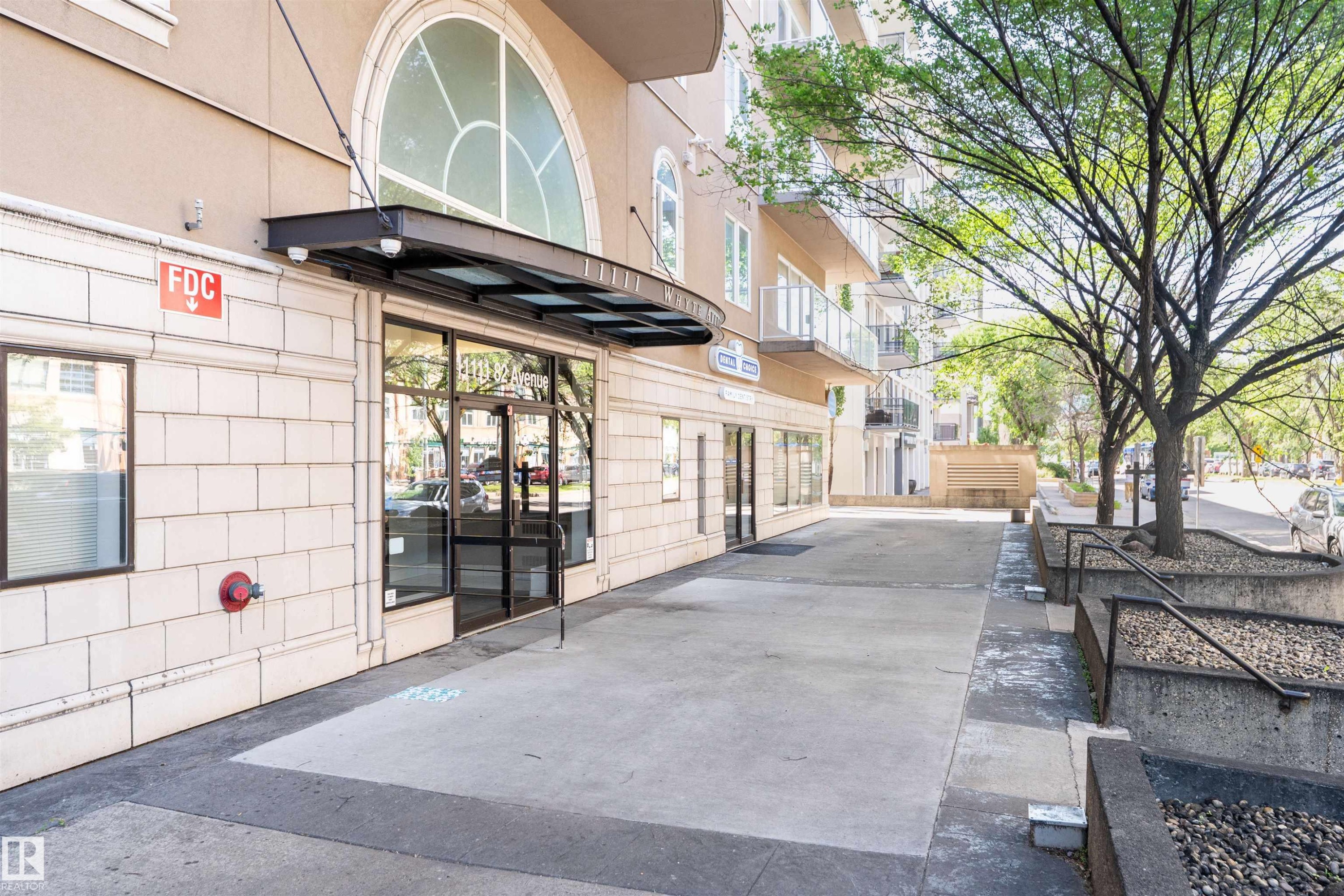 Contemporary building entrance featuring a glass awning, arched transom window, and ground-level retail spaces - 305 11111 82 Avenue, Edmonton, AB
