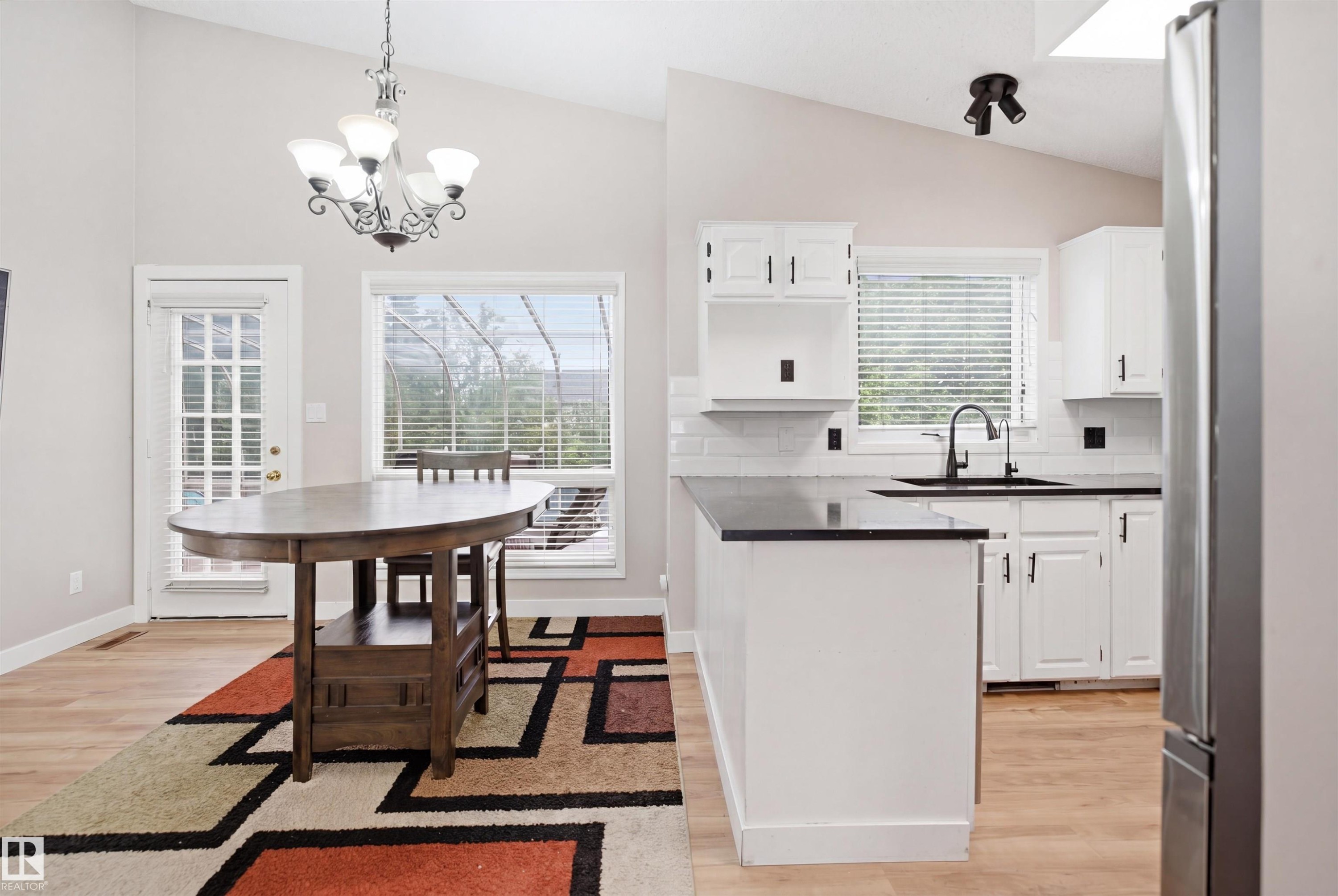 Vaulted ceiling kitchen featuring white cabinetry, a black countertop island, stainless steel refrigerator, and a white subway tile backsplash - 3220 42A Avenue, Edmonton, AB