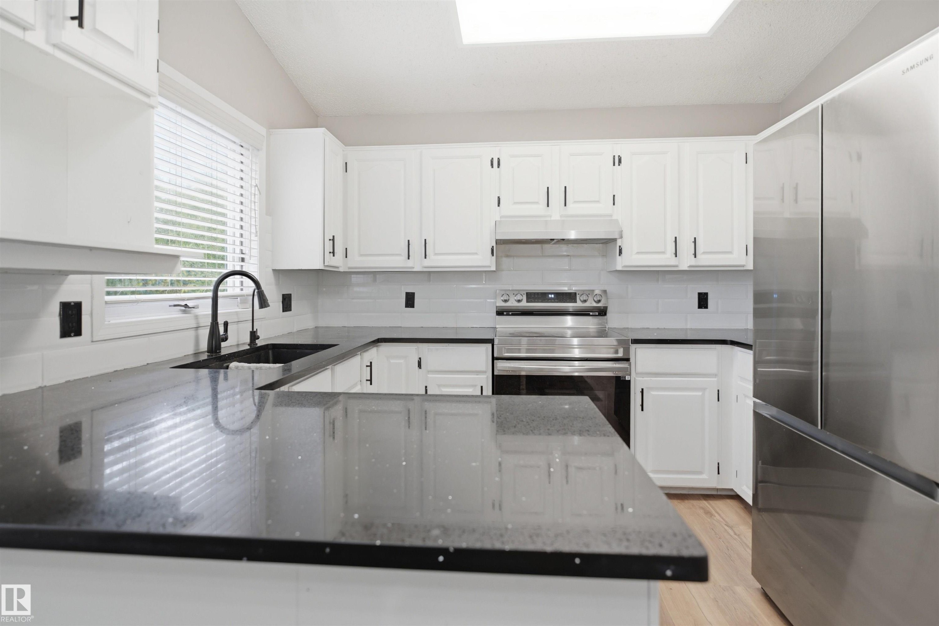 Kitchen featuring dark countertops, white cabinetry, a black faucet, stainless steel appliances, and wood-finish flooring - 3220 42A Avenue, Edmonton, AB