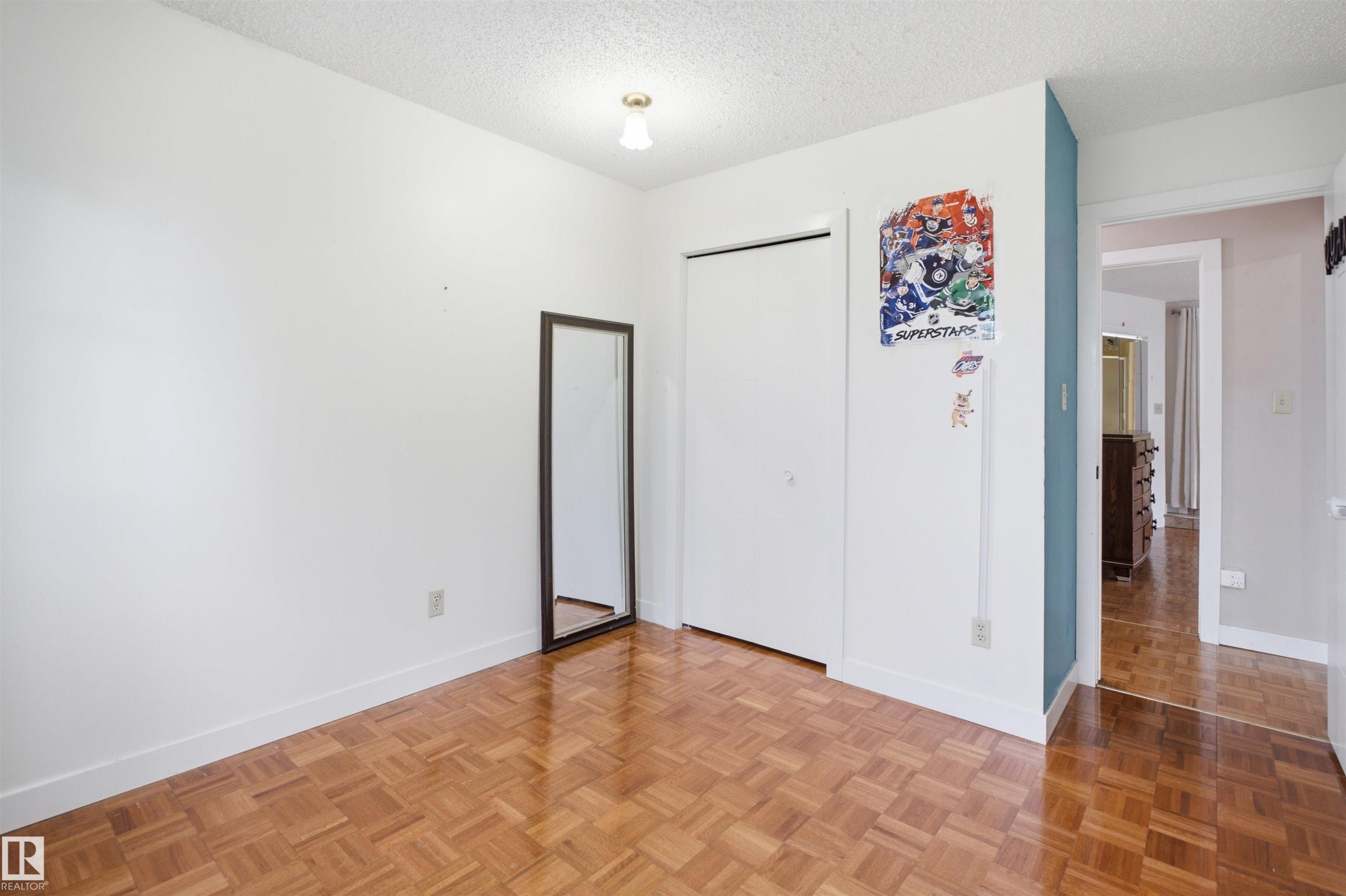 Room featuring wood-finish parquet flooring, white walls, and a built-in closet with bi-fold doors - 3220 42A Avenue, Edmonton, AB