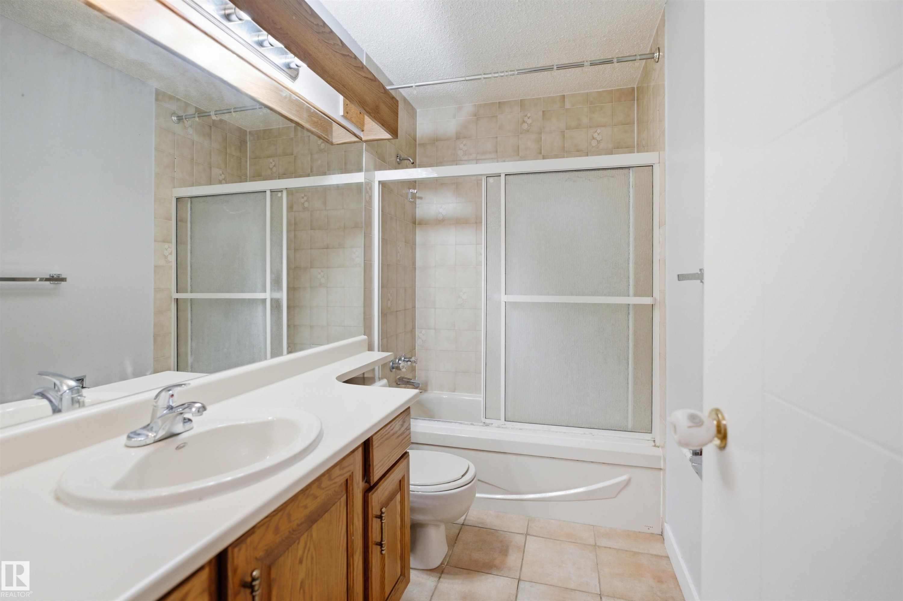 Bathroom featuring a wood-finish vanity with an integrated sink, a large mirror, and a shower-tub combination with sliding frosted glass doors - 3220 42A Avenue, Edmonton, AB
