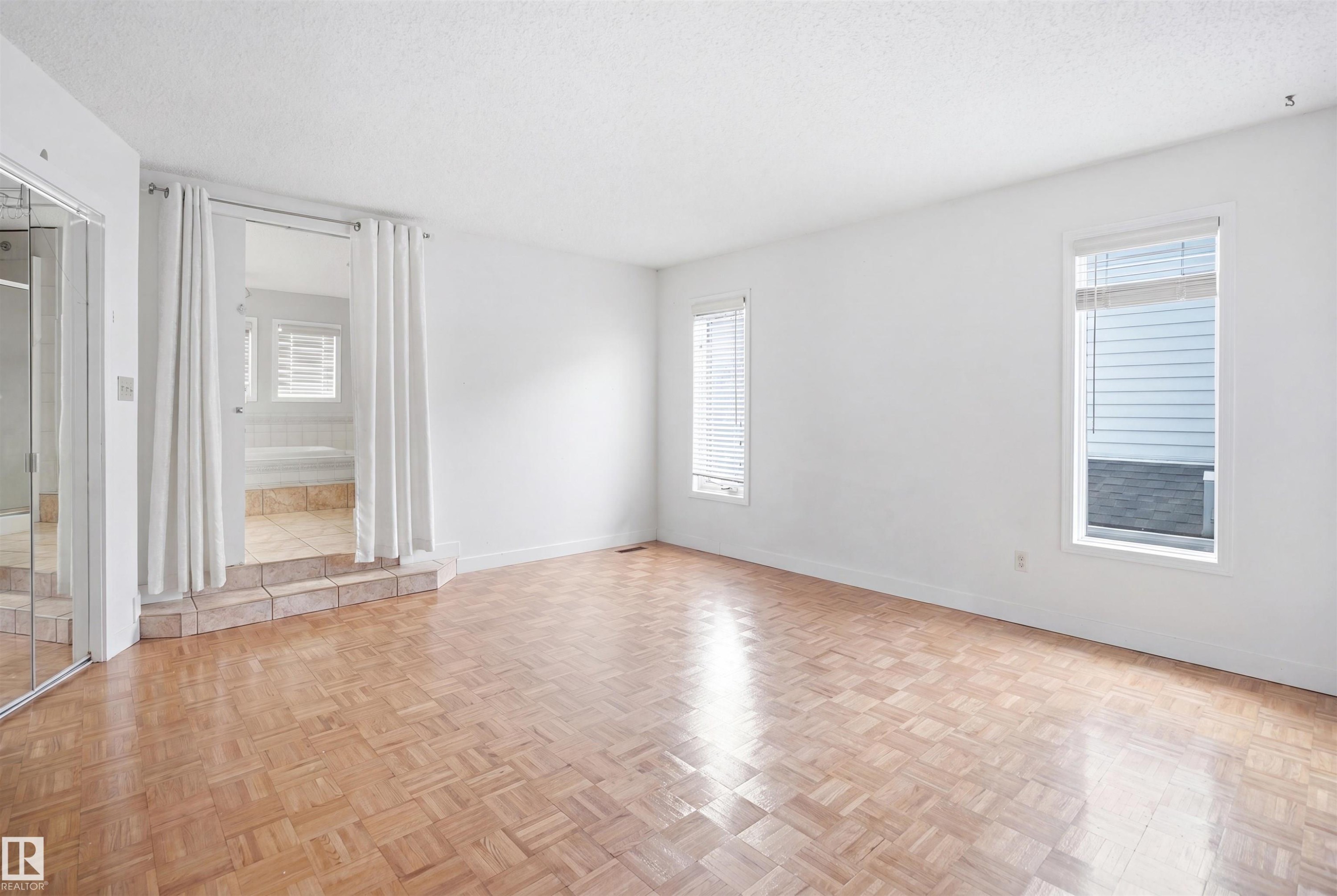 Spacious room featuring wood-finish parquet flooring, multiple windows with blinds, and a mirrored sliding closet door - 3220 42A Avenue, Edmonton, AB