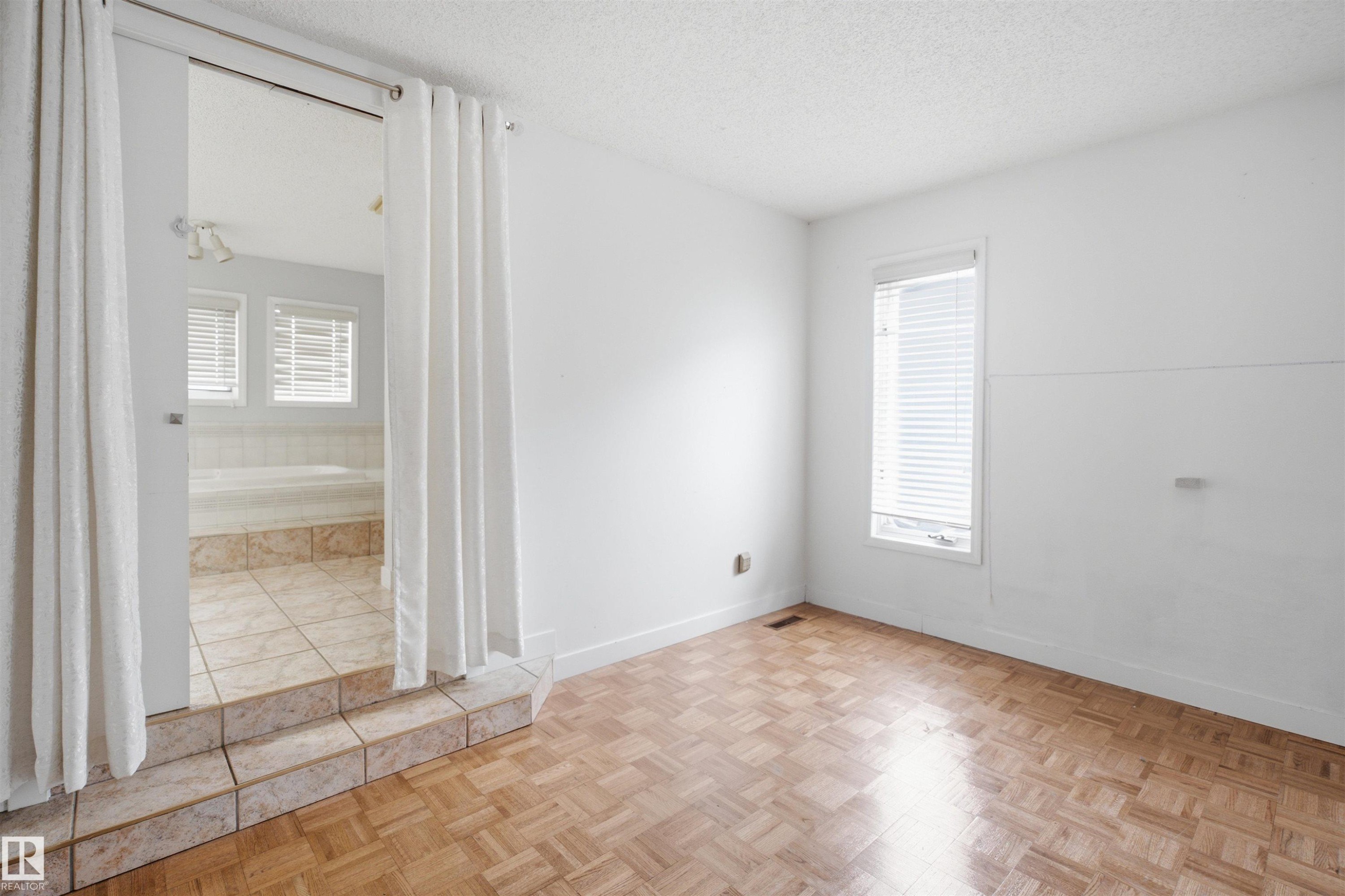 Bedroom featuring parquet wood-finish flooring, a window with horizontal blinds, and direct access to a separate bathing area - 3220 42A Avenue, Edmonton, AB