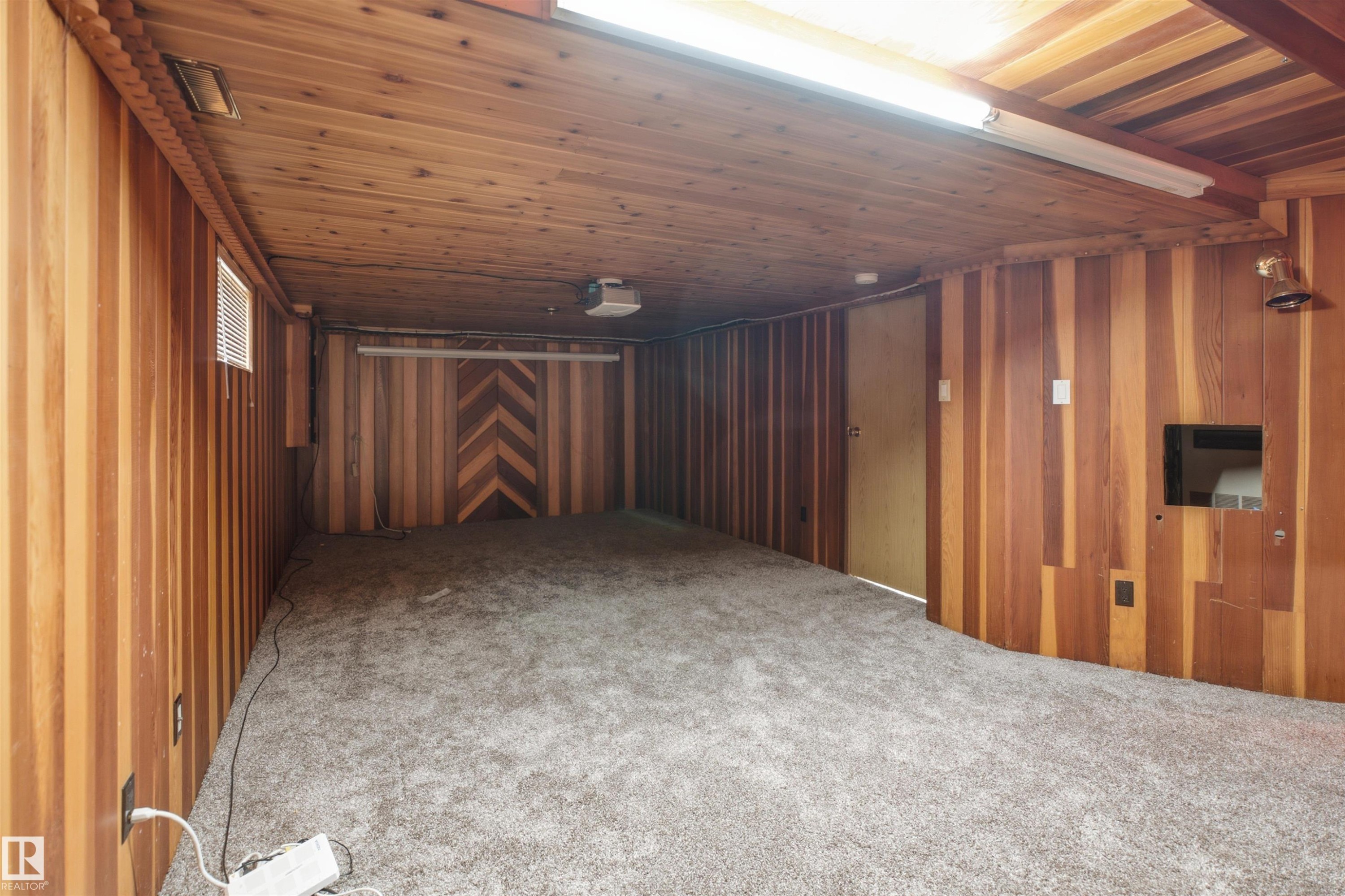 Room featuring wood-paneled walls and ceiling, gray carpet flooring, an integrated projector, and a built-in screen - 3220 42A Avenue, Edmonton, AB