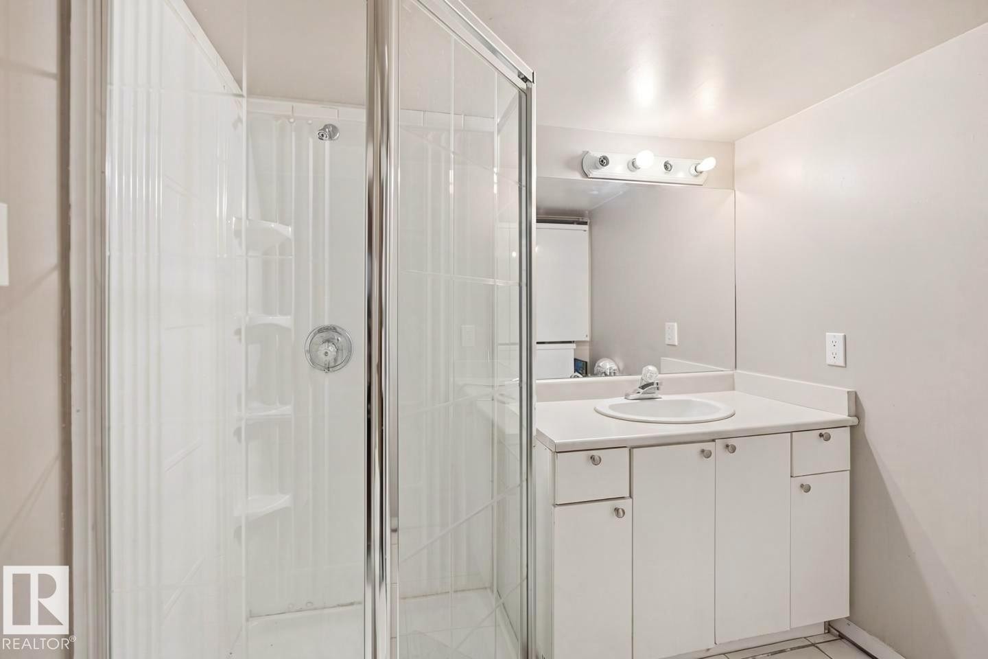Bathroom featuring a glass-enclosed shower, white vanity with integrated sink, white countertop, and wall-mounted mirror with vanity lighting - 3220 42A Avenue, Edmonton, AB