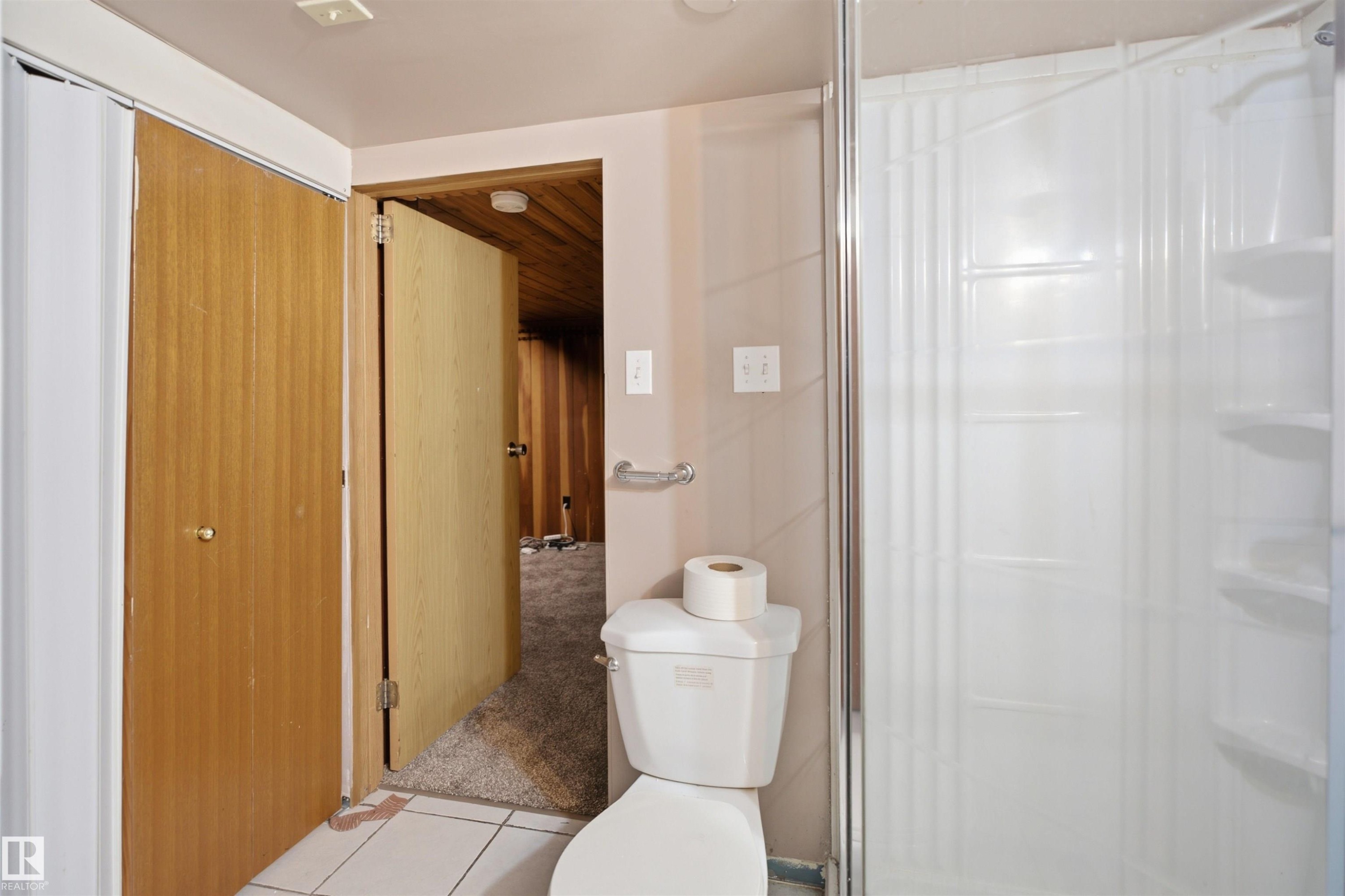Bathroom featuring a white toilet, grab bar, and a shower enclosure with a clear glass door - 3220 42A Avenue, Edmonton, AB