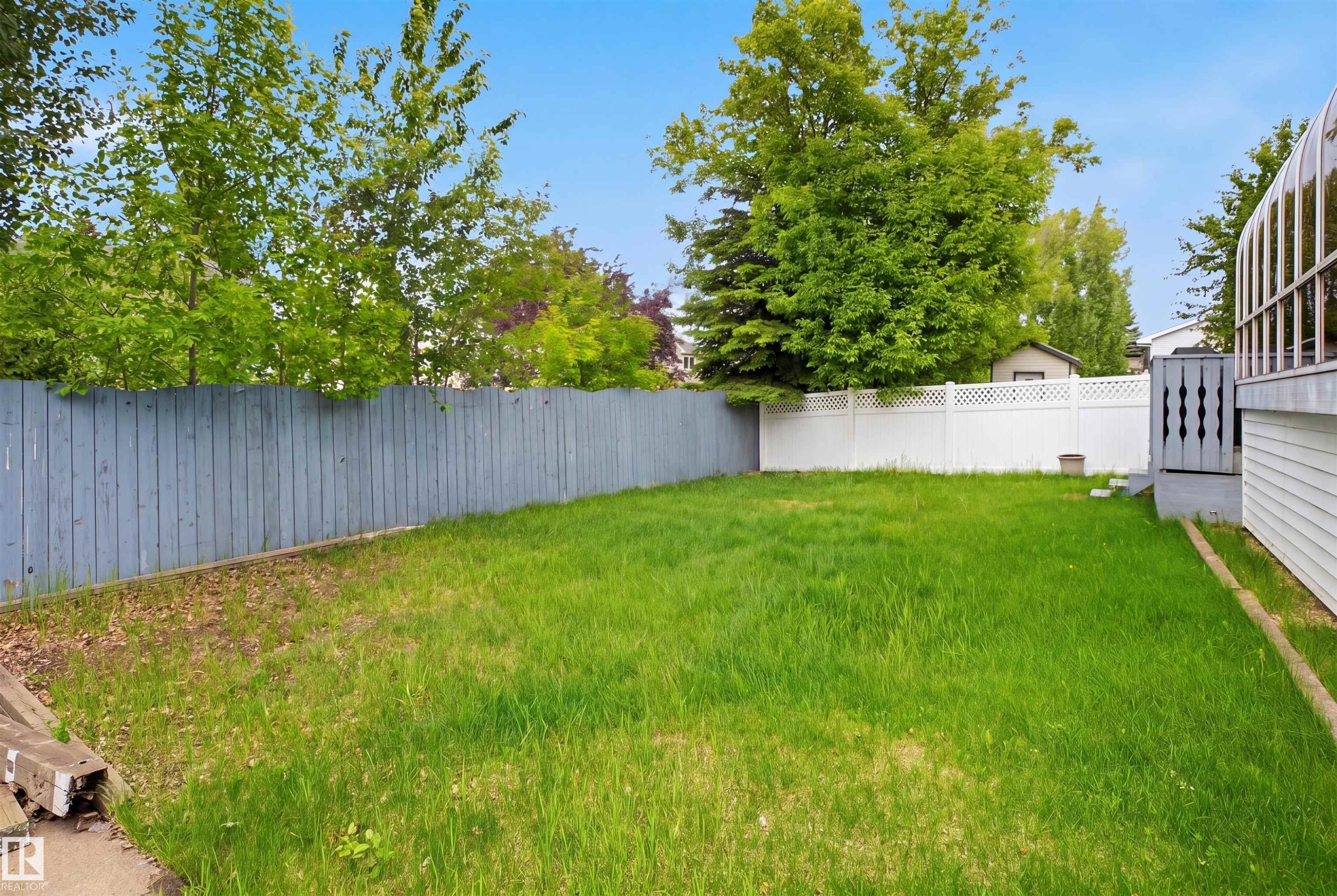 Expansive backyard featuring a large grassy area, a wooden fence, and white lattice fencing - 3220 42A Avenue, Edmonton, AB
