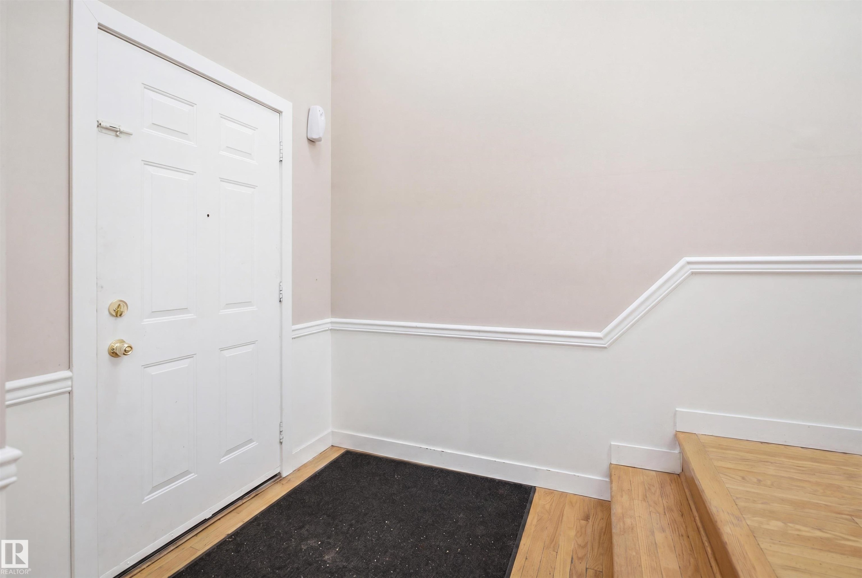 Entryway featuring a white paneled door with brass hardware, wood-finish flooring, and wainscoting with decorative molding - 3220 42A Avenue, Edmonton, AB