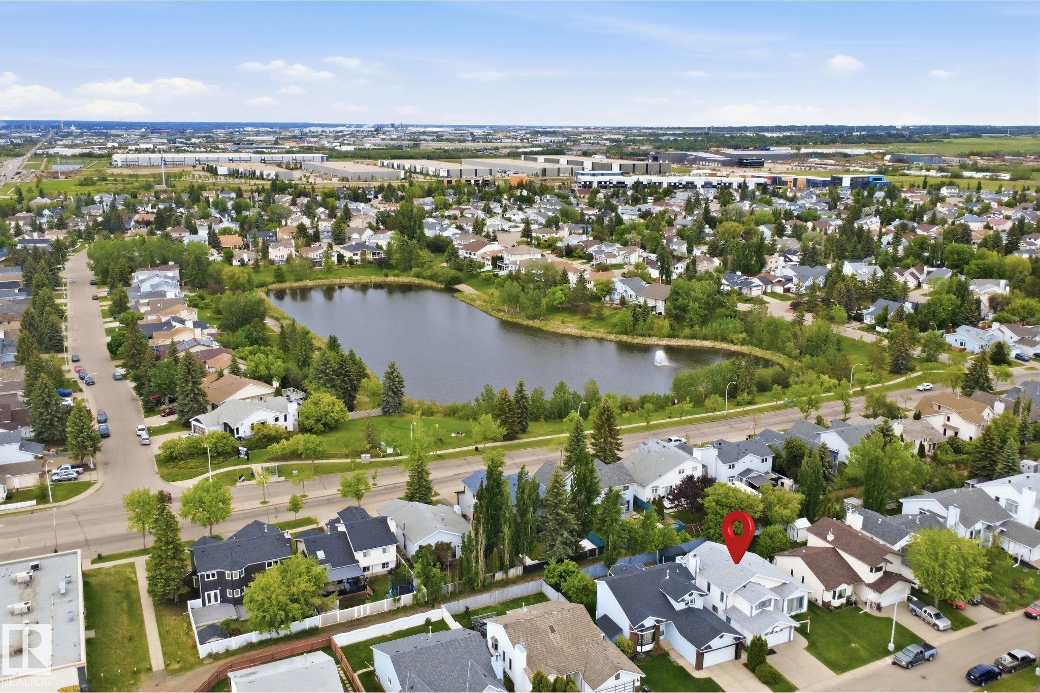 Residential neighborhood featuring a prominent pond with a fountain, surrounded by mature trees and paved roads - 3220 42A Avenue, Edmonton, AB