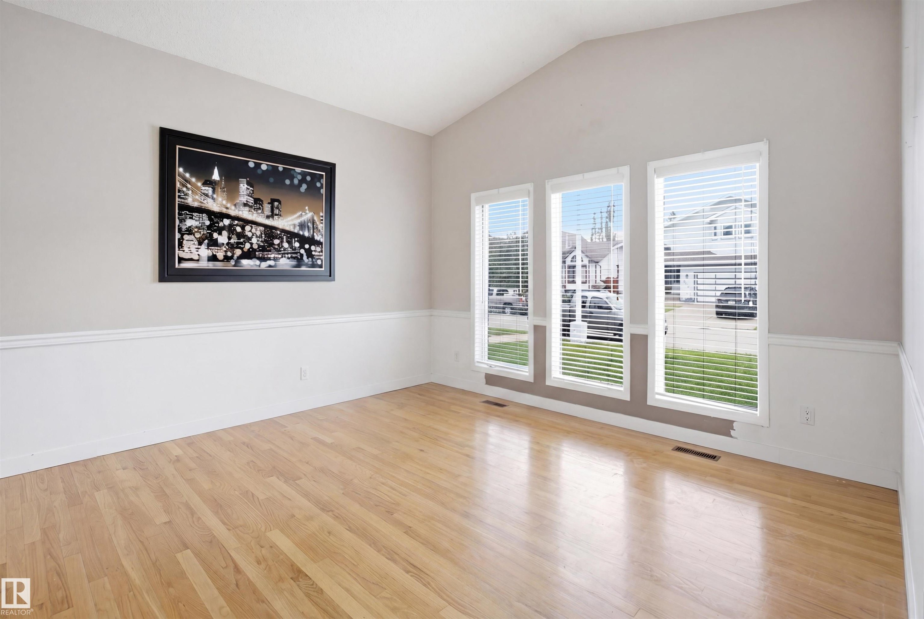Vaulted ceiling room featuring light wood-finish flooring, wainscoting, and three vertical windows with blinds - 3220 42A Avenue, Edmonton, AB