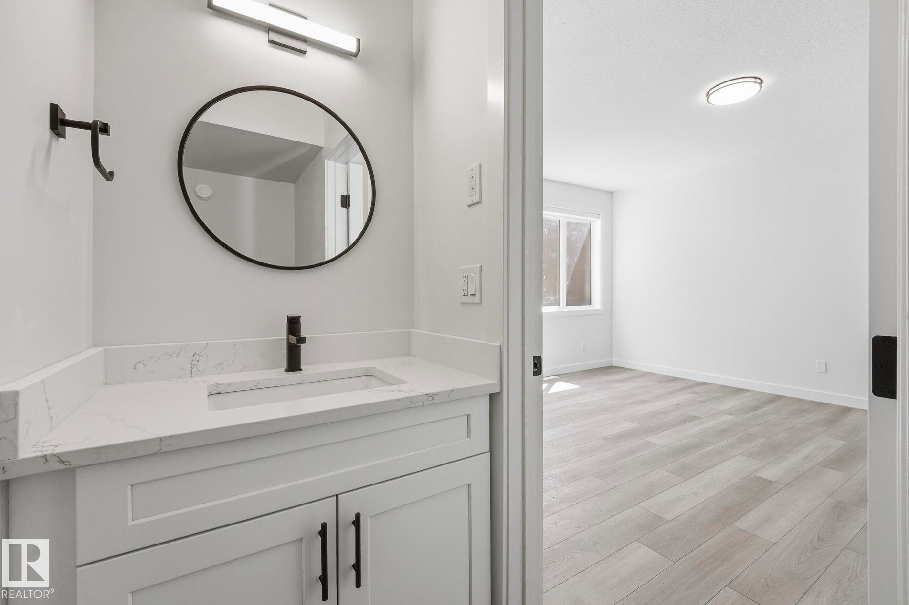 Bathroom vanity featuring a quartz countertop with an integrated sink and matte black faucet - 11012 132 Street, Edmonton, AB