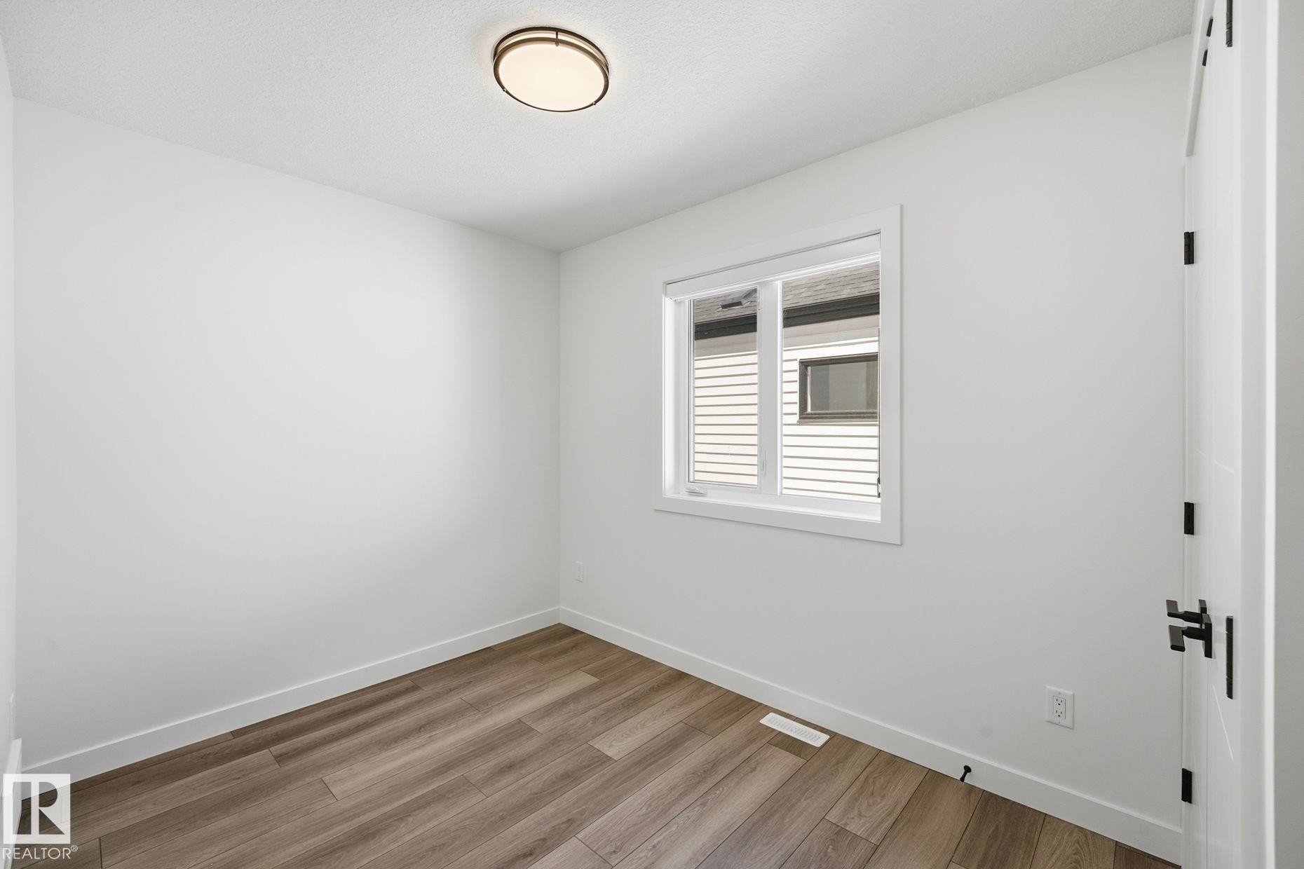 Room featuring wood-finish flooring, white baseboards, and a neutral wall palette - 11012 132 Street, Edmonton, AB