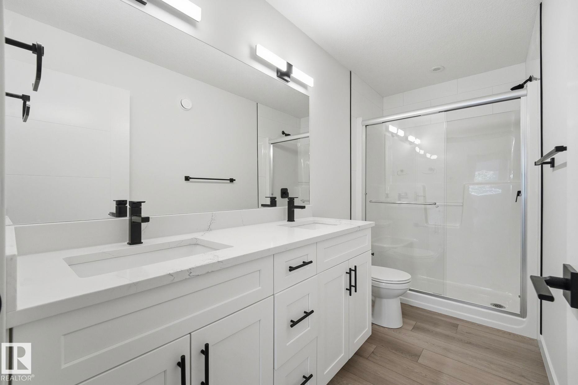 Bathroom featuring a dual vanity with white cabinetry, integrated sinks, and black hardware - 11012 132 Street, Edmonton, AB