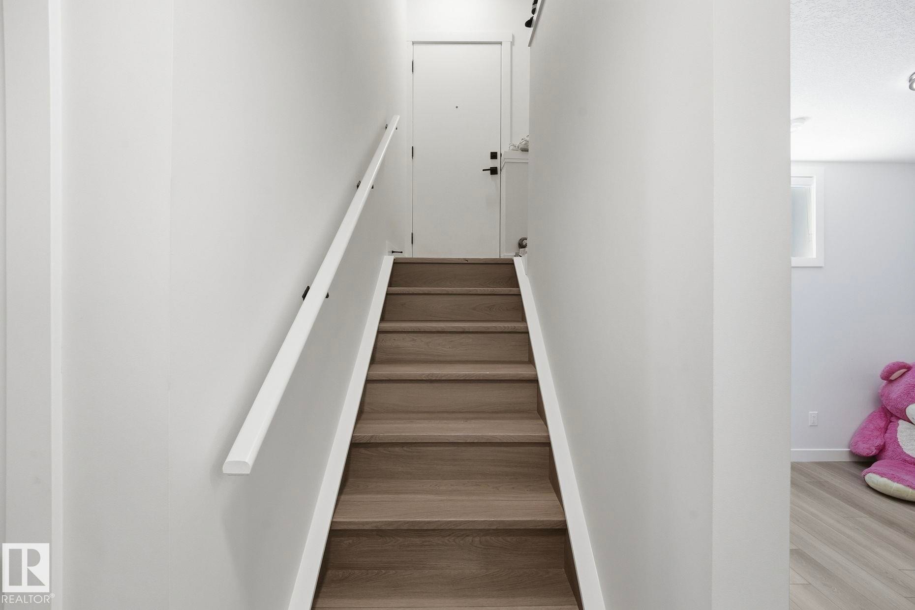 Staircase with wood-finish treads and risers, white walls, and a white handrail with black brackets - 11012 132 Street, Edmonton, AB