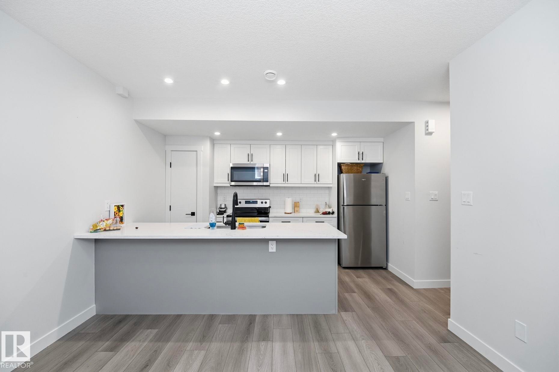 Contemporary kitchen with recessed lighting, white cabinetry, integrated stainless steel appliances, a breakfast bar, and wood-finish flooring - 11012 132 Street, Edmonton, AB