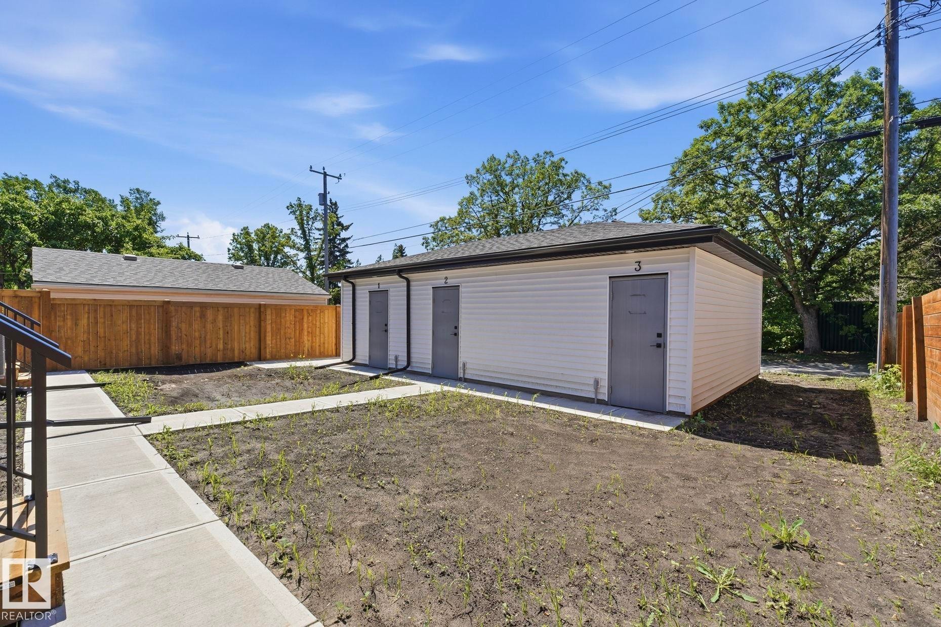 Detached auxiliary building featuring three numbered exterior doors, white siding, and a dark shingle roof - 11012 132 Street, Edmonton, AB