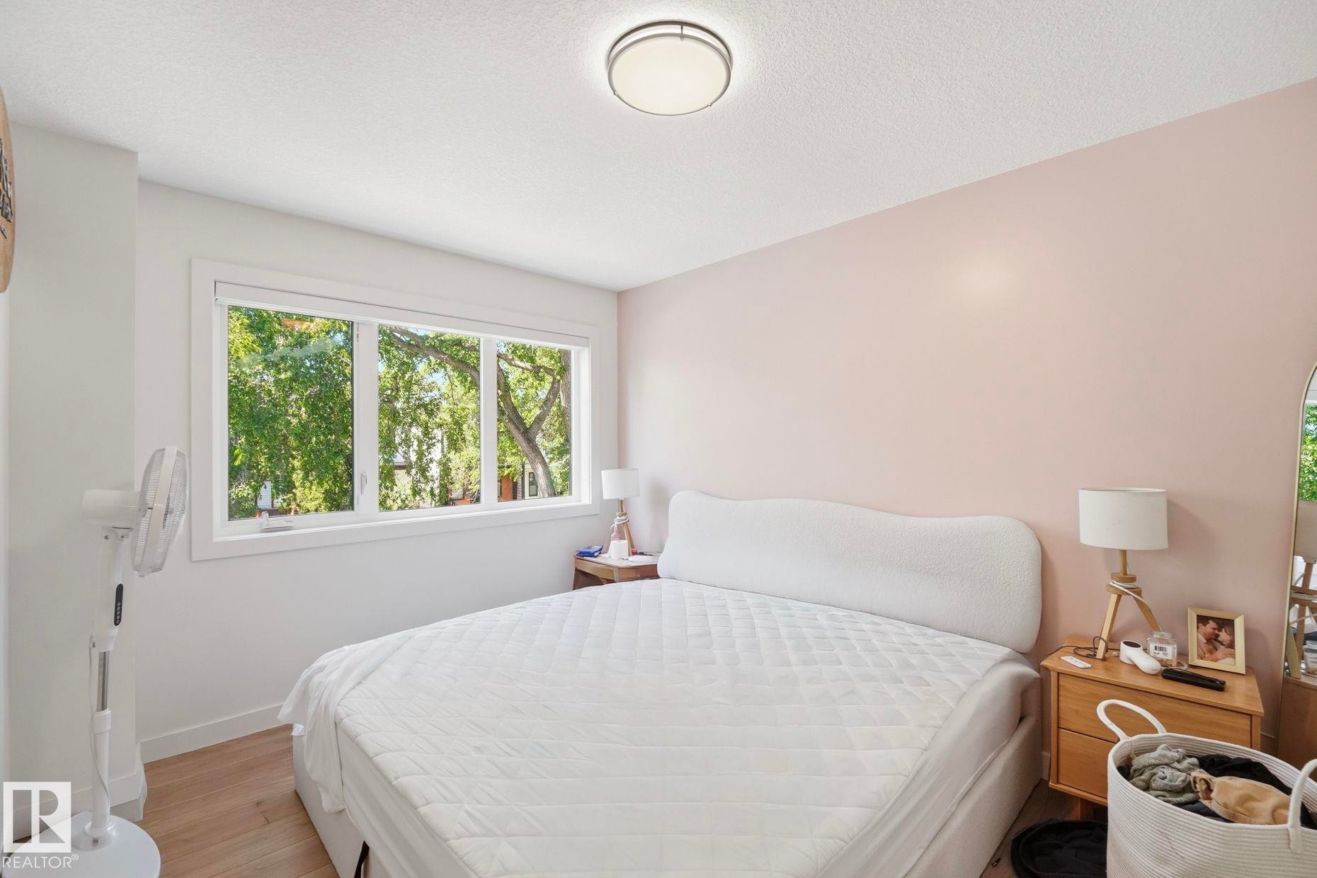 Bedroom featuring a large multi-pane window, light pink wall accent, ceiling-mounted light fixture, and wood-finish flooring - 11007 132 Street, Edmonton, AB