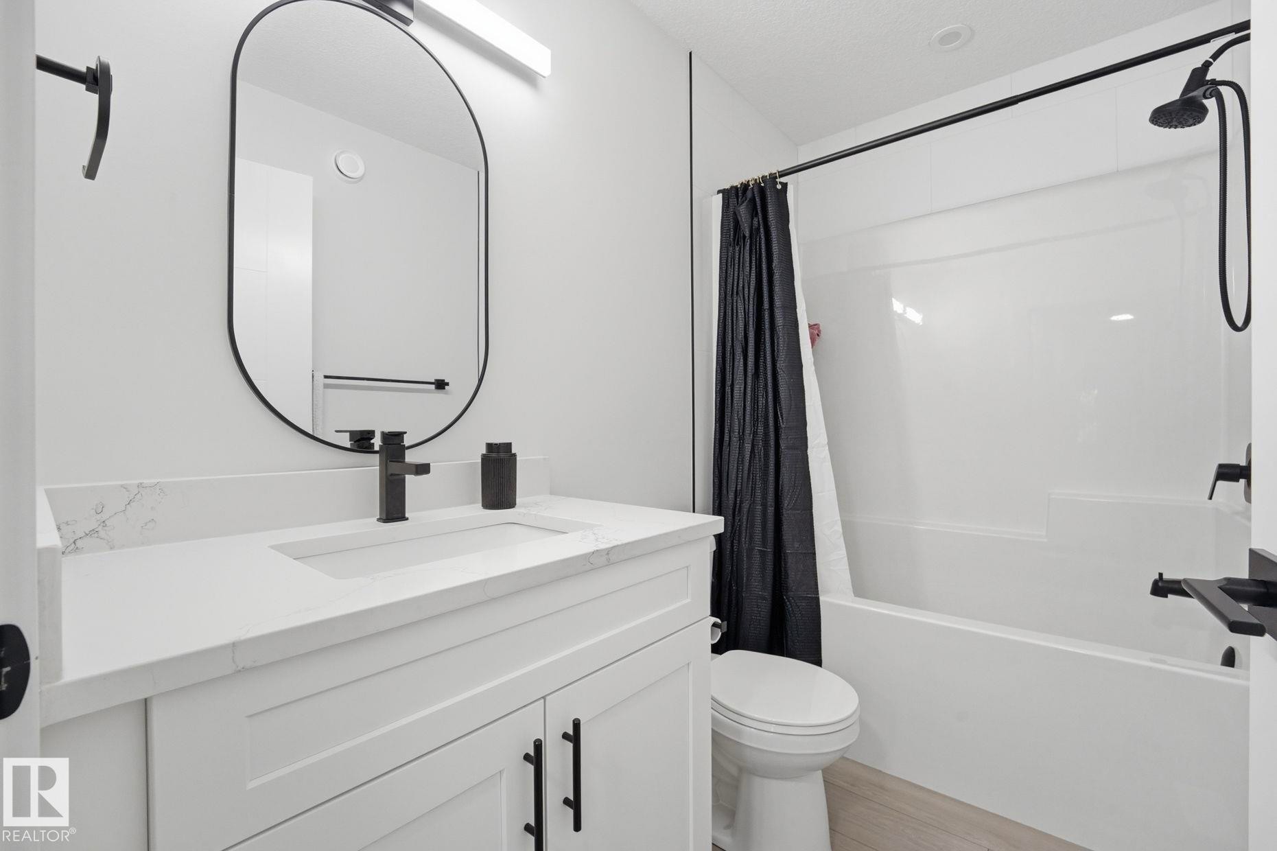 Bathroom featuring a single vanity with stone-finish countertop, undermount sink, and matte black faucet - 11007 132 Street, Edmonton, AB