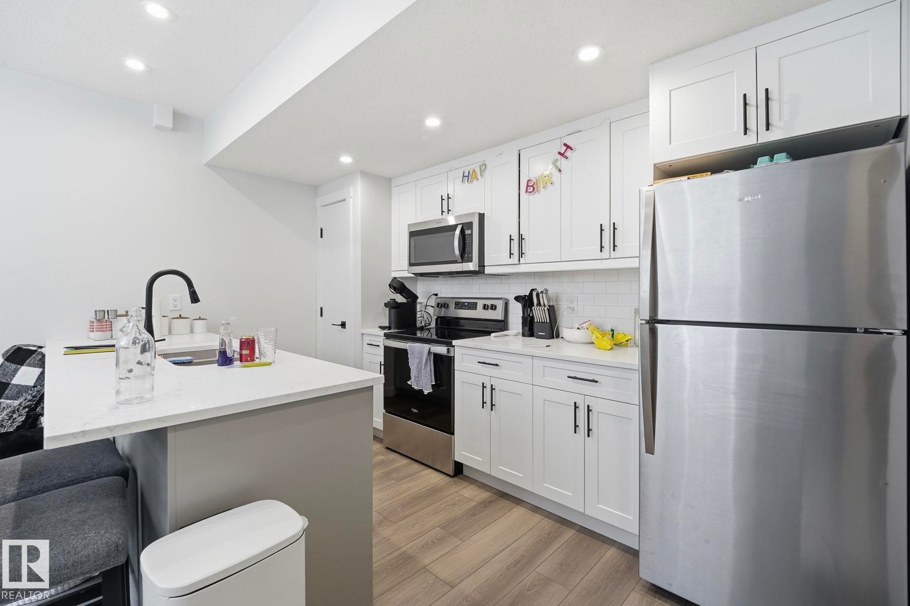 Contemporary kitchen featuring white shaker cabinetry with dark hardware, stainless steel appliances, and wood-finish flooring - 11007 132 Street, Edmonton, AB