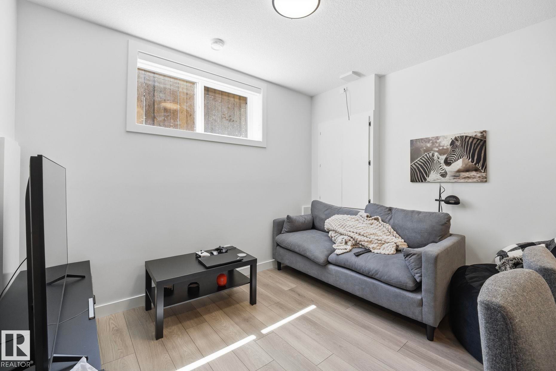 Finished basement living space featuring light wood-finish flooring, a contemporary window, and recessed lighting - 11007 132 Street, Edmonton, AB